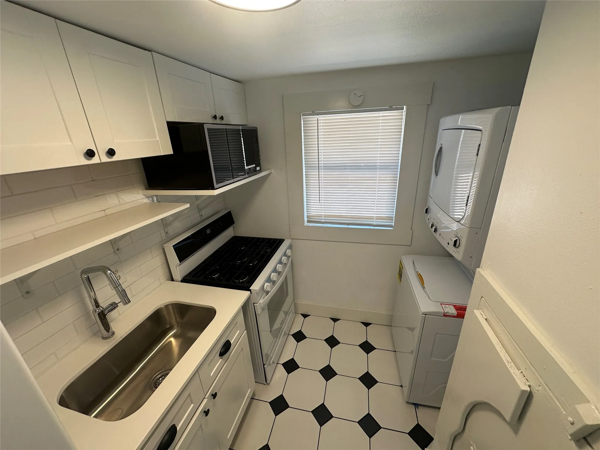 Compact kitchen featuring white cabinetry, a gas range, a stainless steel sink, and geometric floor tiling