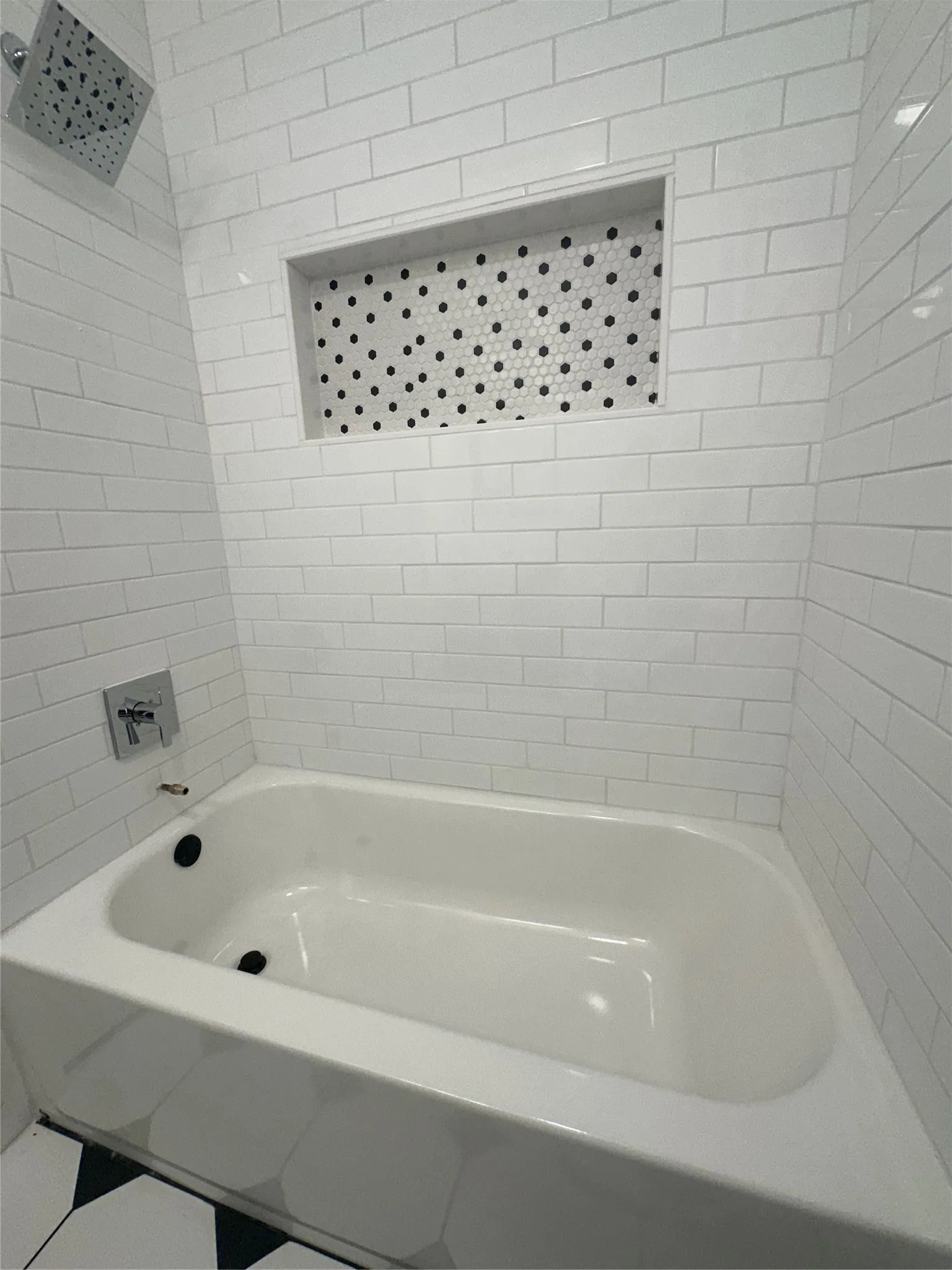 Bathtub with subway tile surround, built-in recessed shelf with hexagon mosaic tile, rain showerhead, and polished chrome fixtures