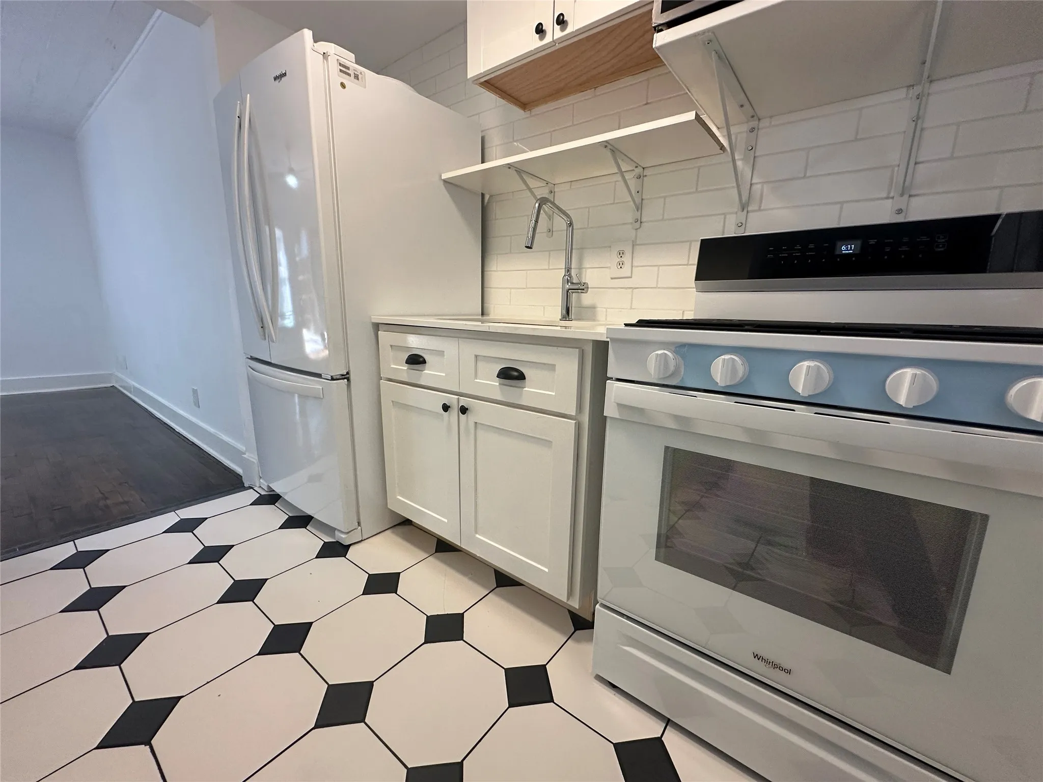 Kitchen featuring white shaker cabinetry, patterned floor tiling, subway tile backsplash, and stainless steel appliances