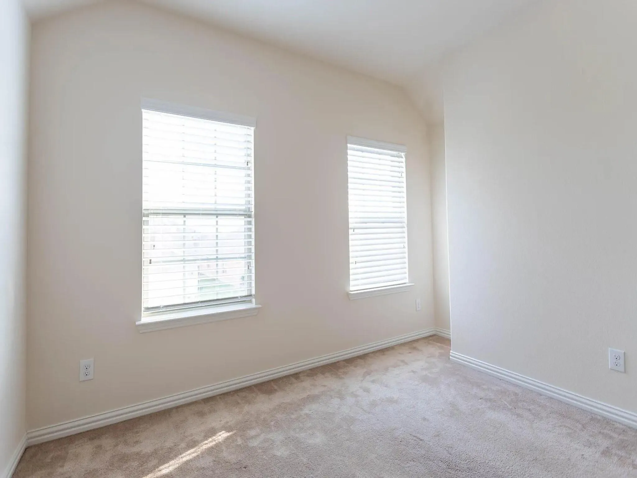 Carpeted room featuring two windows with blinds, light-toned walls, and sloped ceiling details