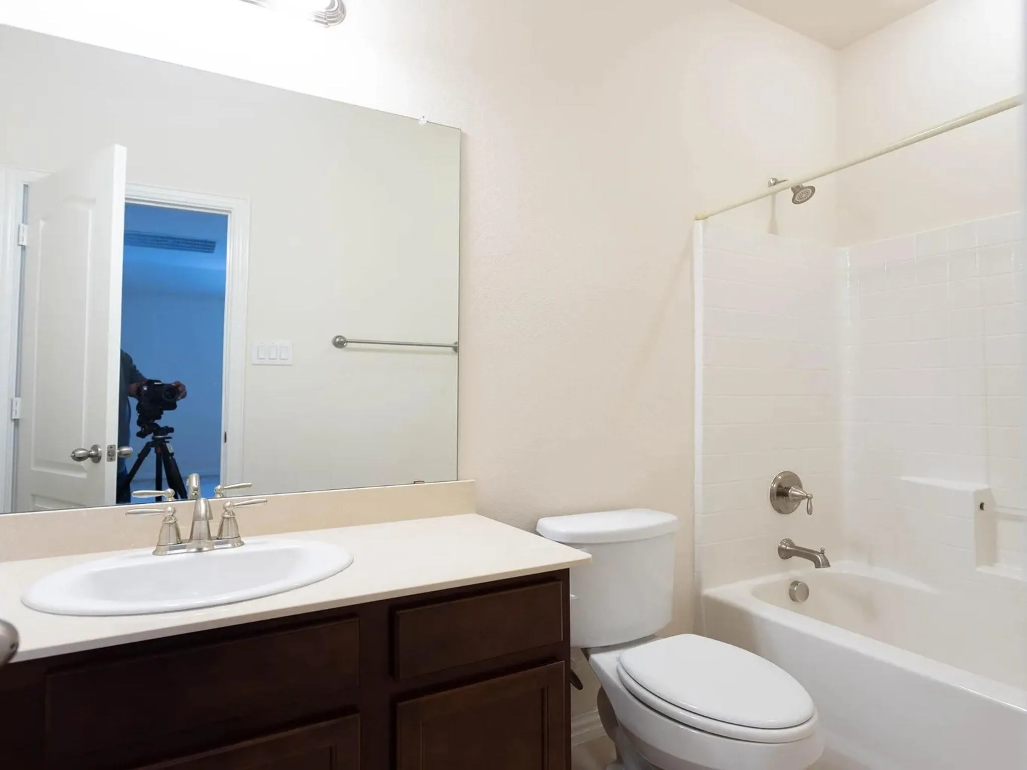 Bathroom featuring a dark wood-finish vanity with an integrated sink, a single-handle brushed nickel faucet, a full-width mirror, and a shower-tub combination with white tile surround