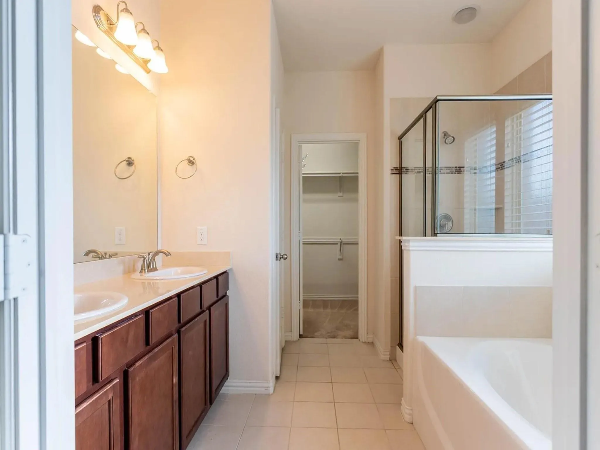 Dual vanity with undermount sinks and wood cabinetry, a built-in soaking tub, and a separate glass-enclosed shower