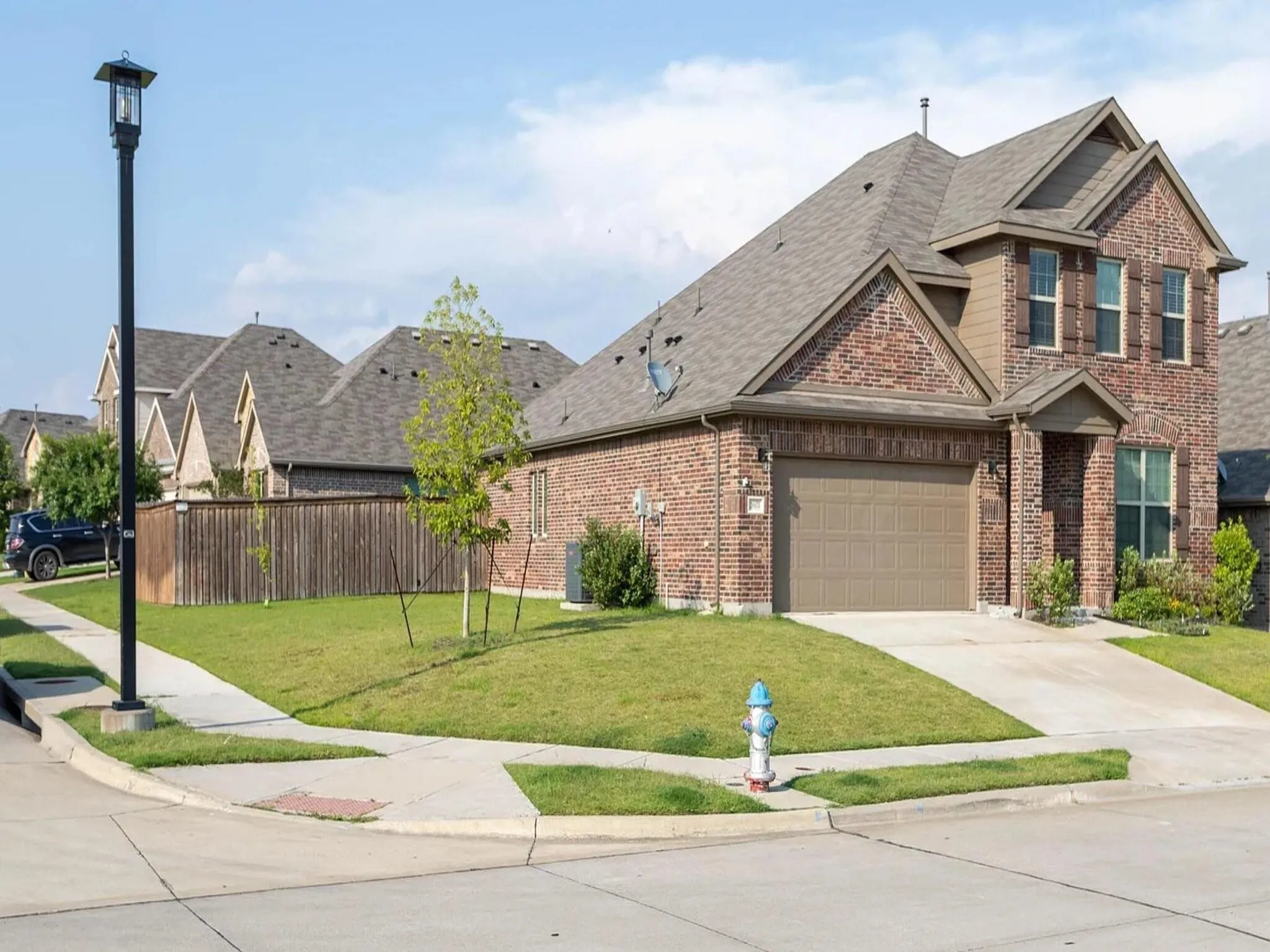 Brick exterior with contrasting brown siding accents, attached two-car garage, covered entry, and a manicured lawn