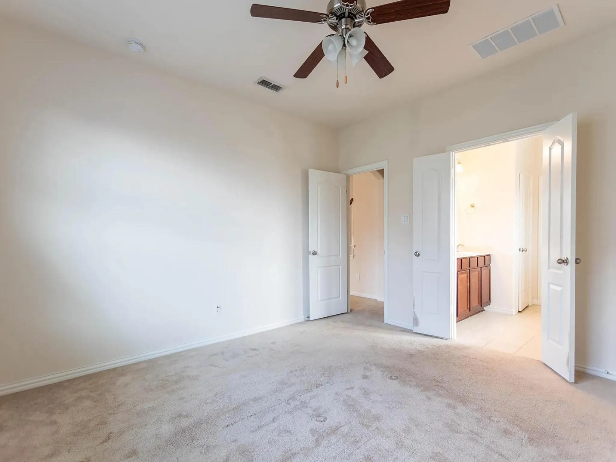Neutral tone wall paint, carpet flooring, and a ceiling fan with integrated lighting