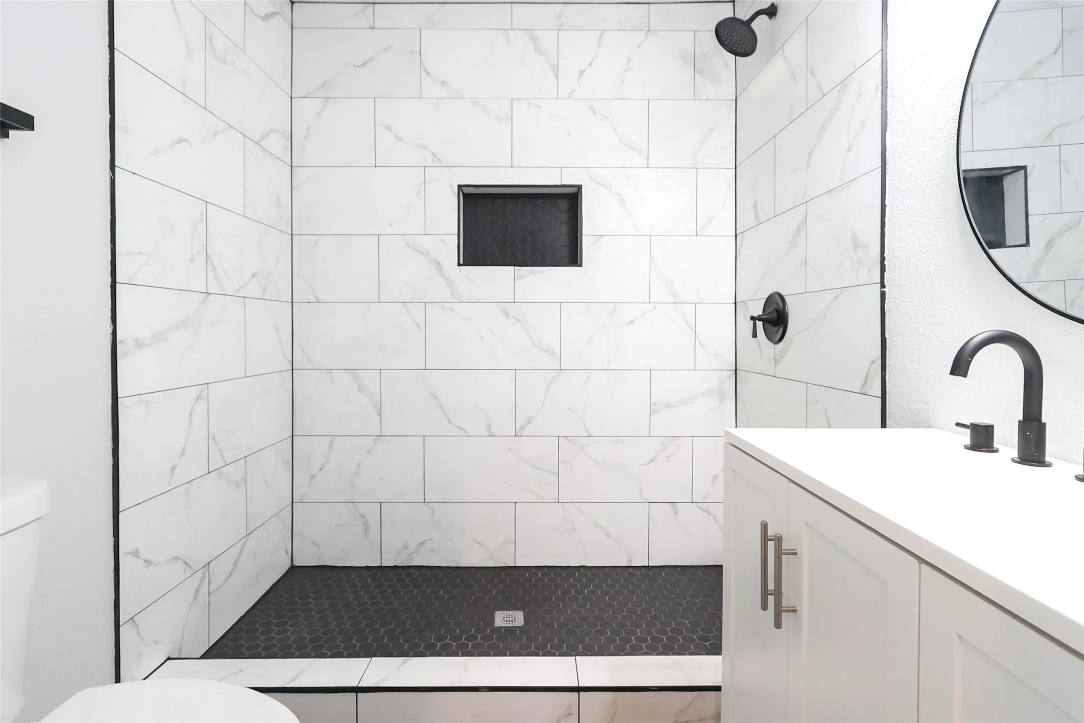 Shower with white marble-patterned subway tile walls, a built-in niche, and a dark hexagonal tile floor