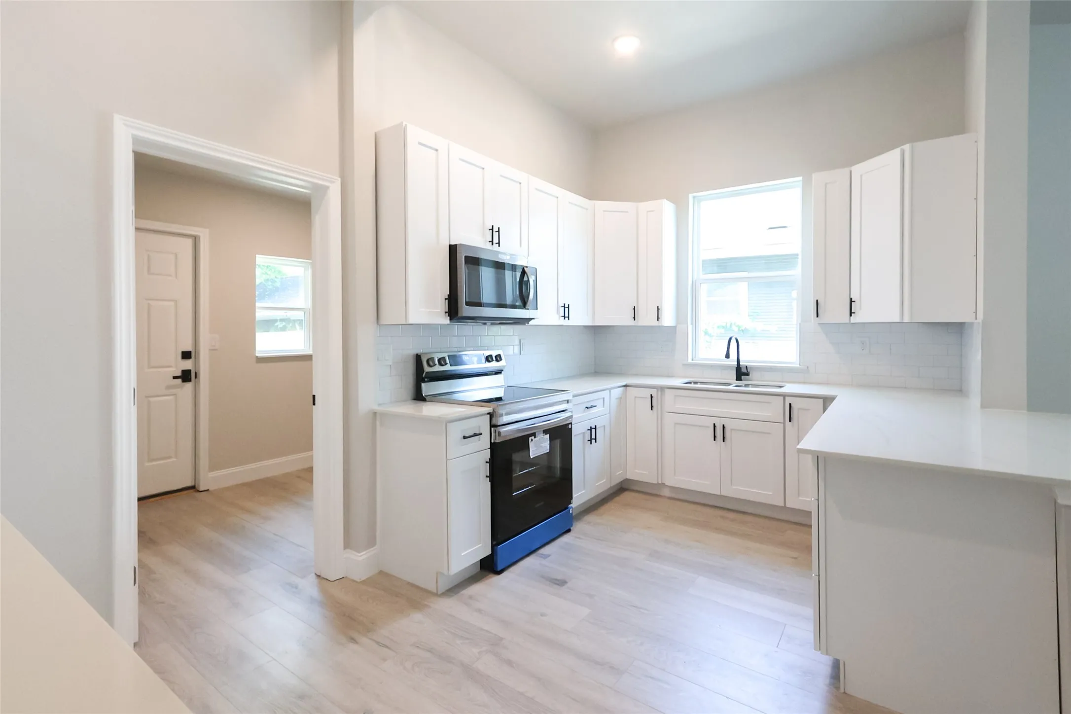 Kitchen featuring white cabinetry, light-toned countertops, a subway tile backsplash, stainless steel appliances, and wood-finish flooring