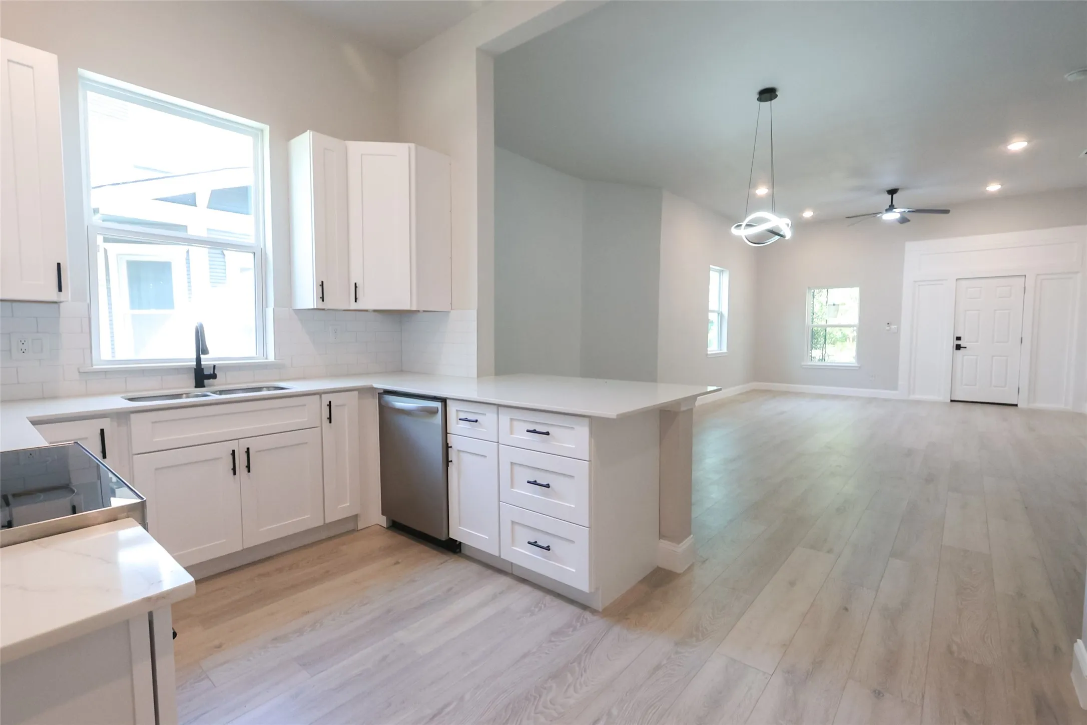Open-concept living space featuring wood-finish flooring, white shaker cabinetry, stainless steel appliances, and a kitchen island with stone countertops