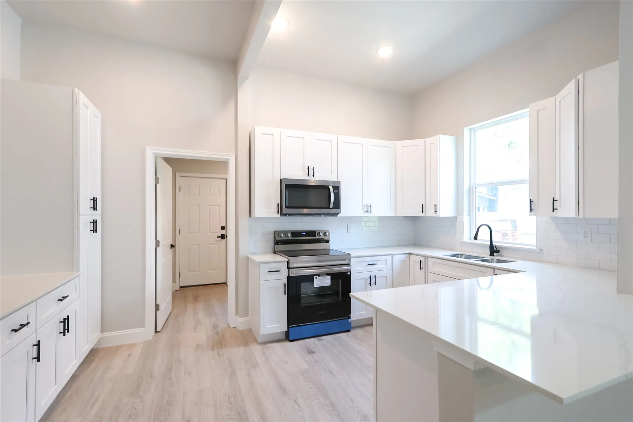 Kitchen featuring white cabinetry, light-toned countertops, a subway tile backsplash, stainless steel appliances, and wood-finish flooring