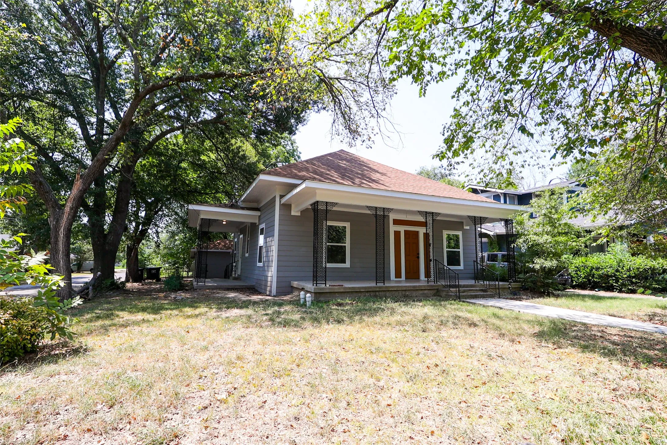 Craftsman-style exterior with a covered porch, wood-finish front door, gray siding, and mature trees