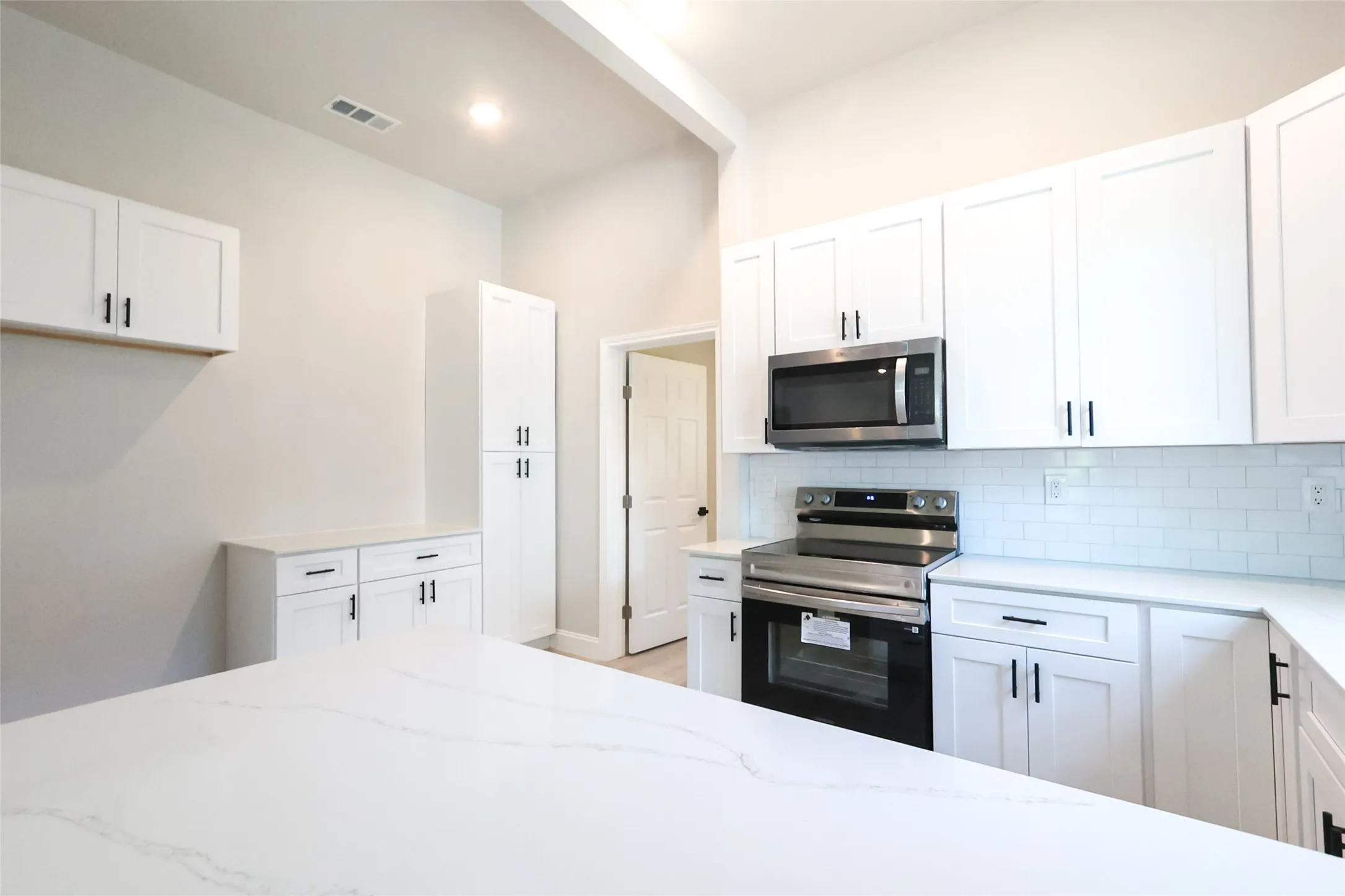Kitchen featuring white shaker cabinetry, stainless steel appliances, a subway tile backsplash, and light-toned countertops