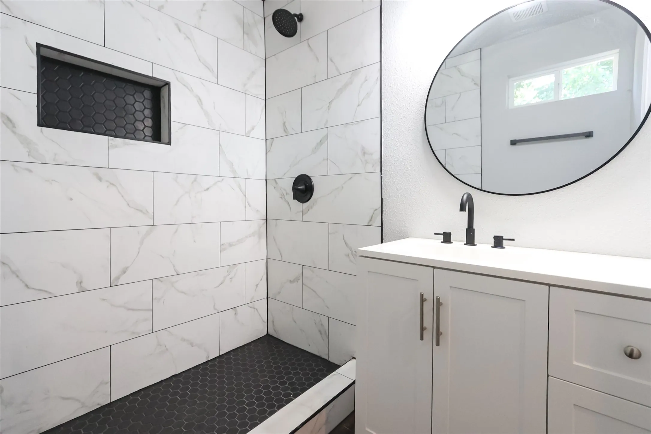 White vanity with a solid surface countertop, matte black fixtures, and an oval mirror