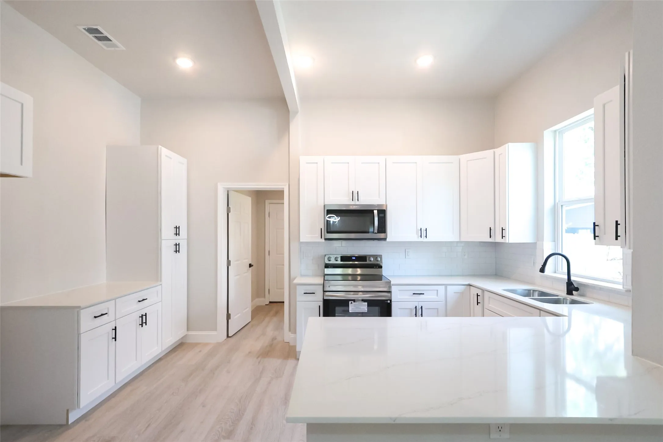 White shaker cabinetry, light-toned wood-finish flooring, recessed lighting, white subway tile backsplash, and a stainless steel appliance suite