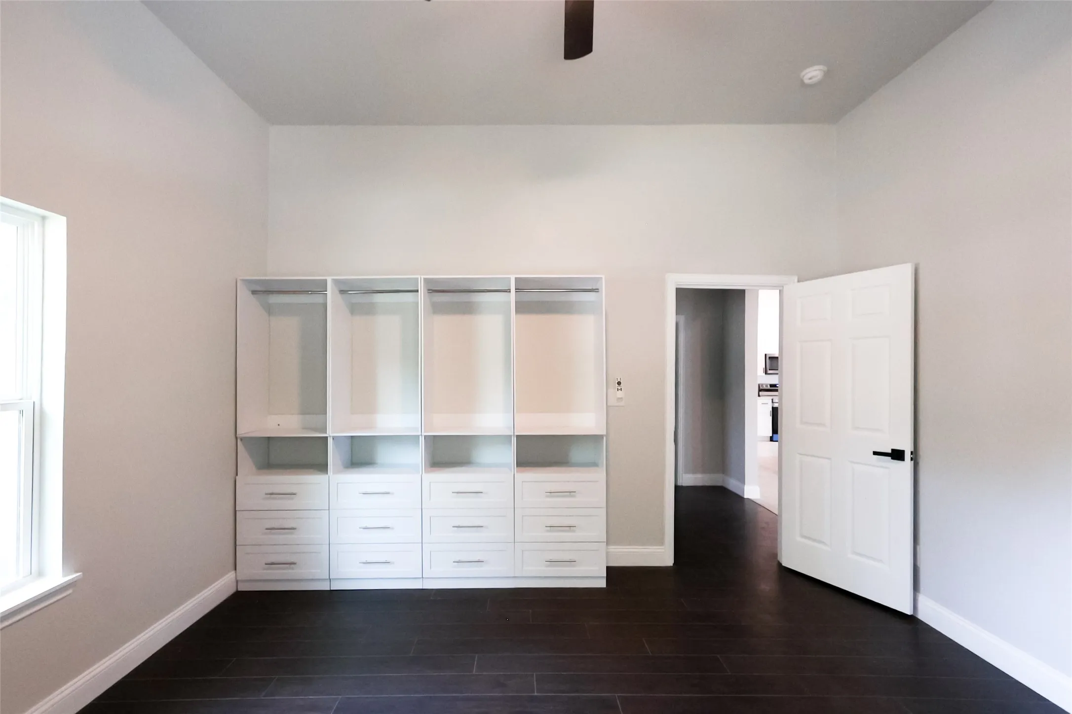 Vaulted ceiling with a ceiling fan, built-in white cabinetry with drawers and shelving, dark wood-finish flooring, and a paneled interior door with matte black hardware