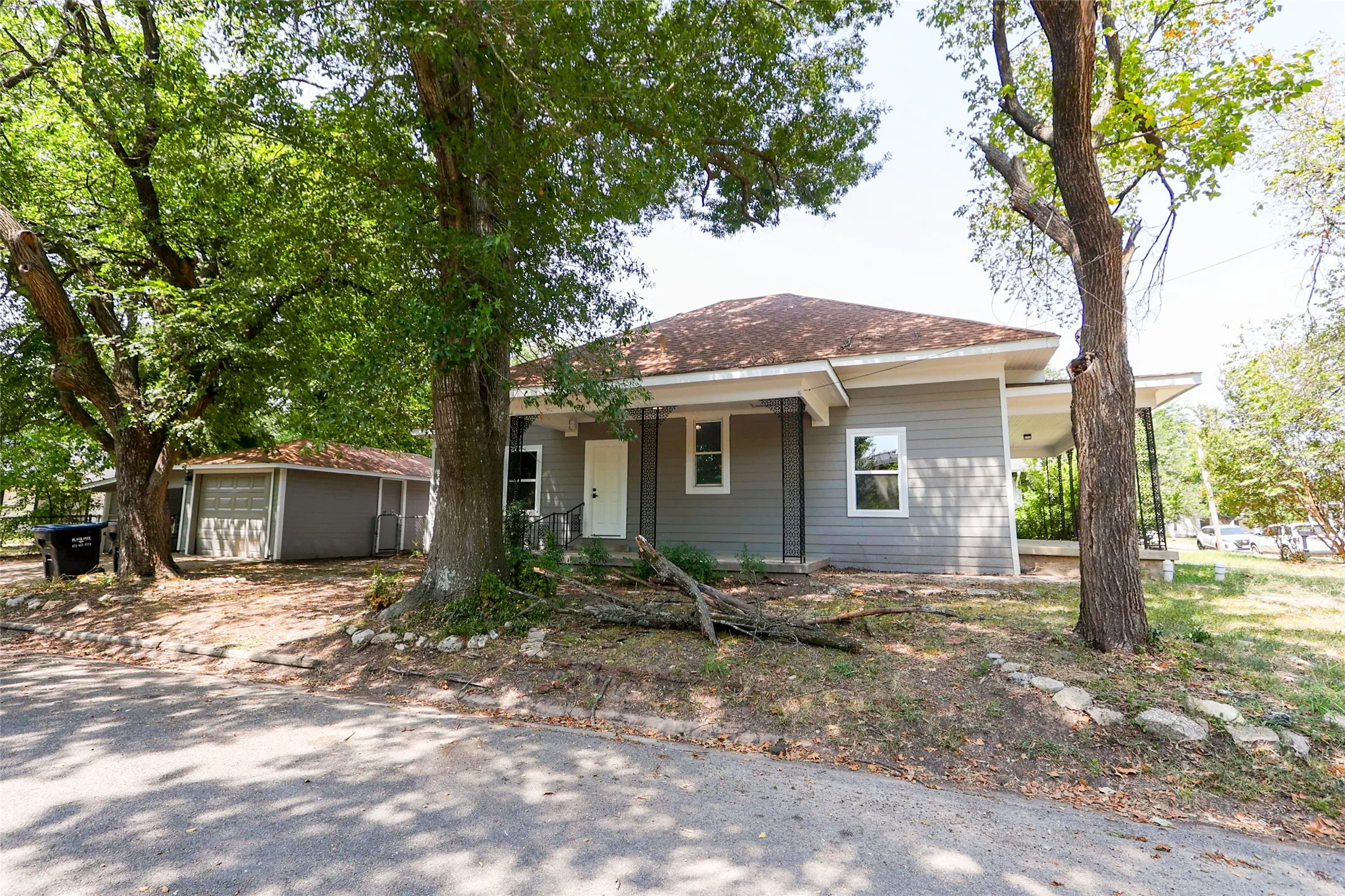 Siding exterior with a covered porch, mature trees, and a detached garage featuring a roll-up door