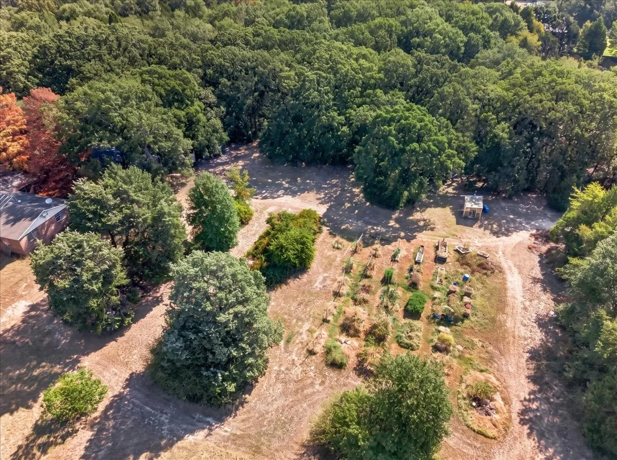Expansive wooded grounds featuring a cultivated garden area, mature trees, and a detached outbuilding