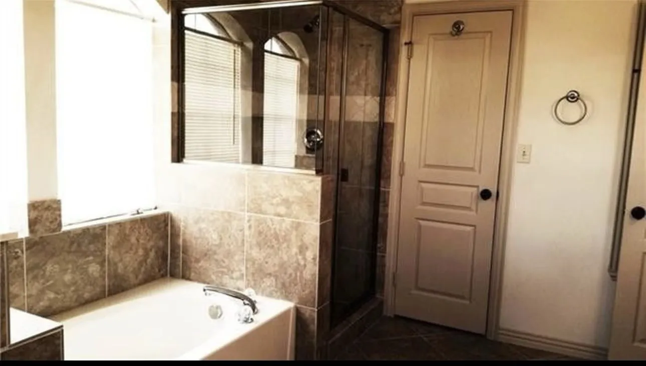 Soaking tub with tile surround, glass-enclosed shower, and arched window with blinds