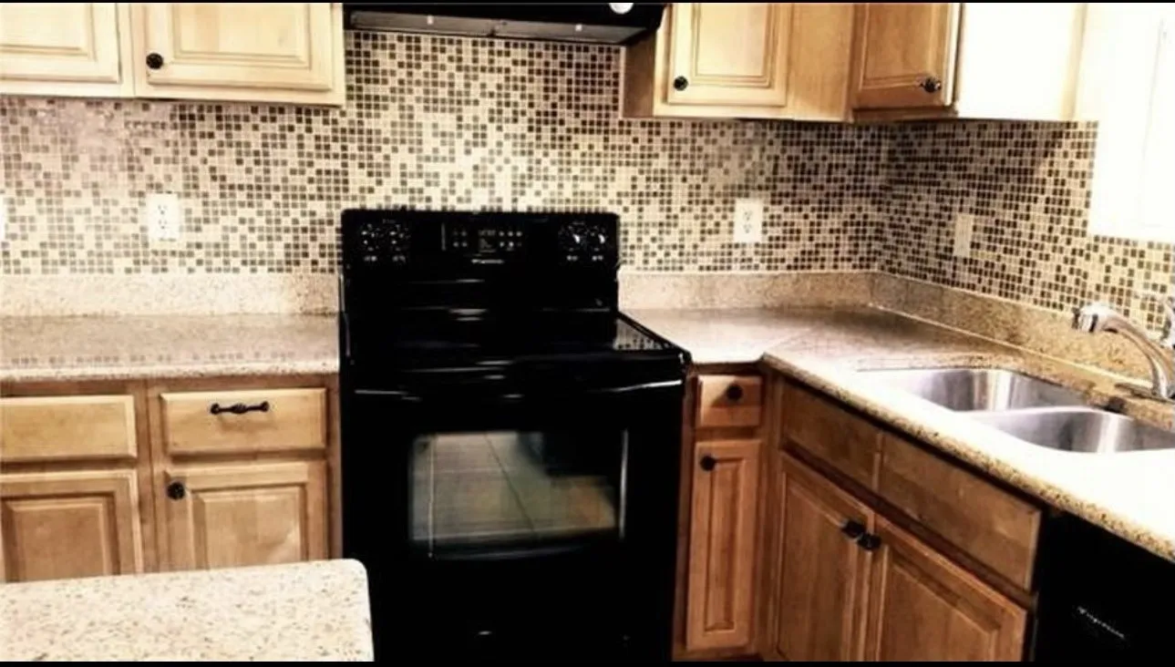 Kitchen featuring natural wood cabinetry, mosaic tile backsplash, solid surface countertops, a black range, and a double basin stainless steel sink