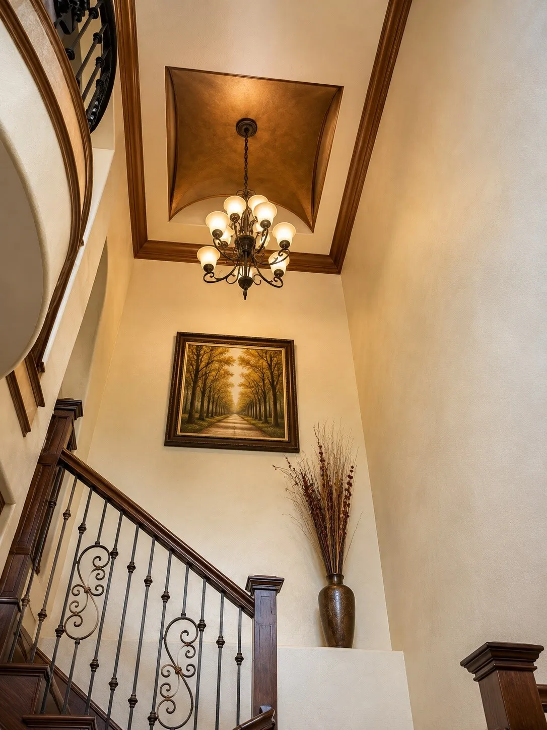 Two-story foyer featuring an ornate chandelier, coffered ceiling with a detailed finish, and a grand staircase with dark wood-finish handrails and decorative iron balusters