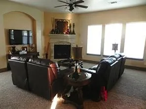 Living area featuring a ceiling fan, carpeted flooring, a fireplace with a mantel, an arched wall niche, and three windows