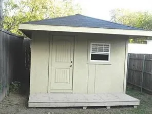 Detached structure with a pitched roof, exterior paneling, a single entry door, and a window with horizontal blinds