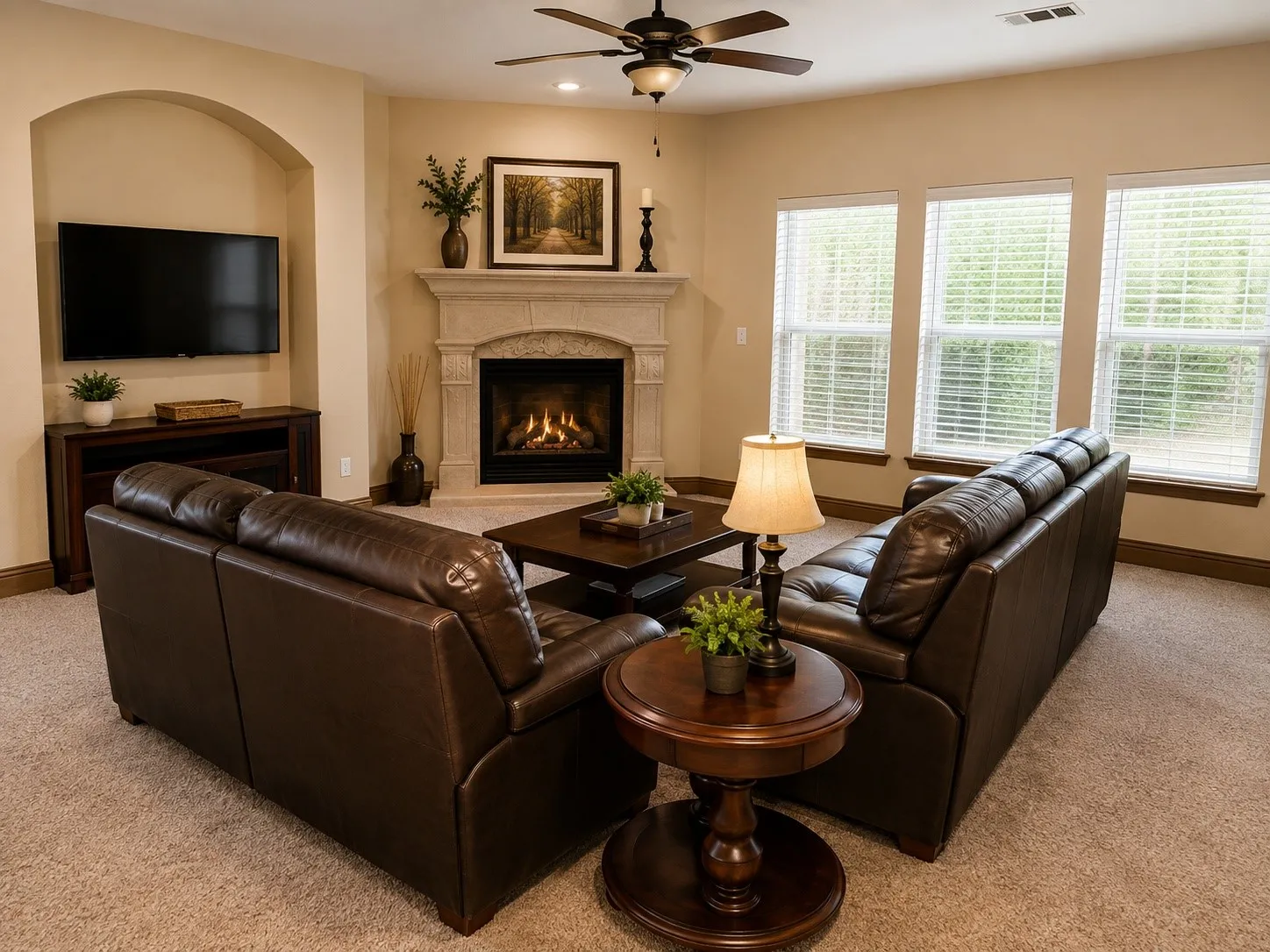 Built-in media niche, corner fireplace with stone mantel, three large windows with blinds, ceiling fan, and carpet flooring