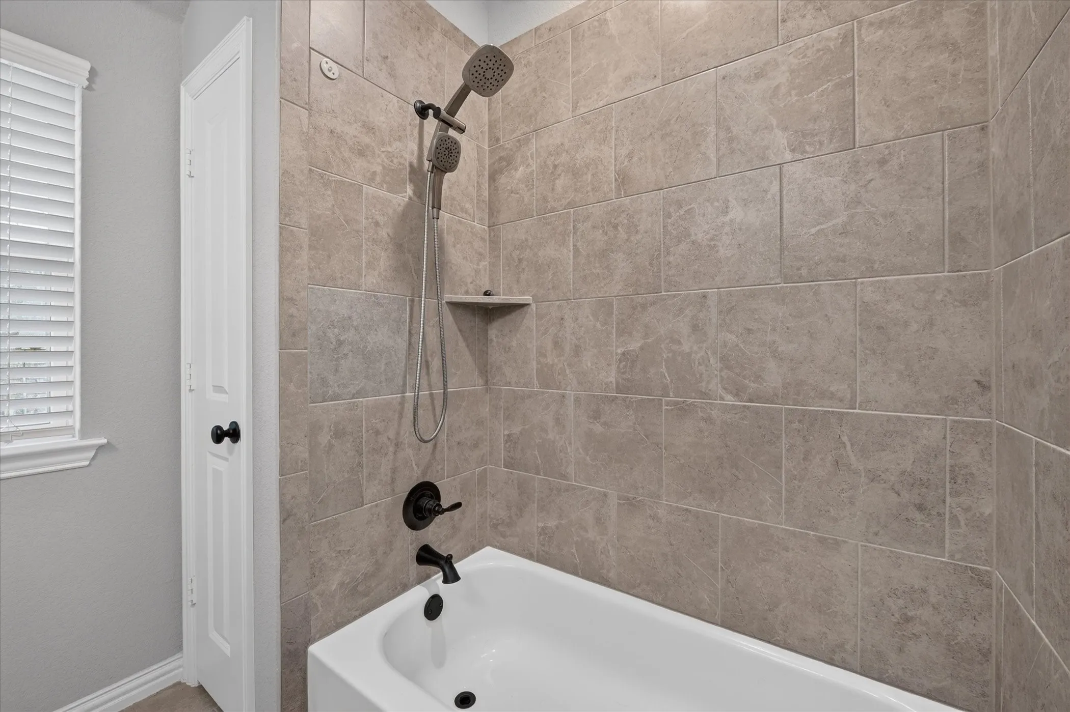 White tub with dark bronze fixtures, subway tile surround, and a built-in shower niche