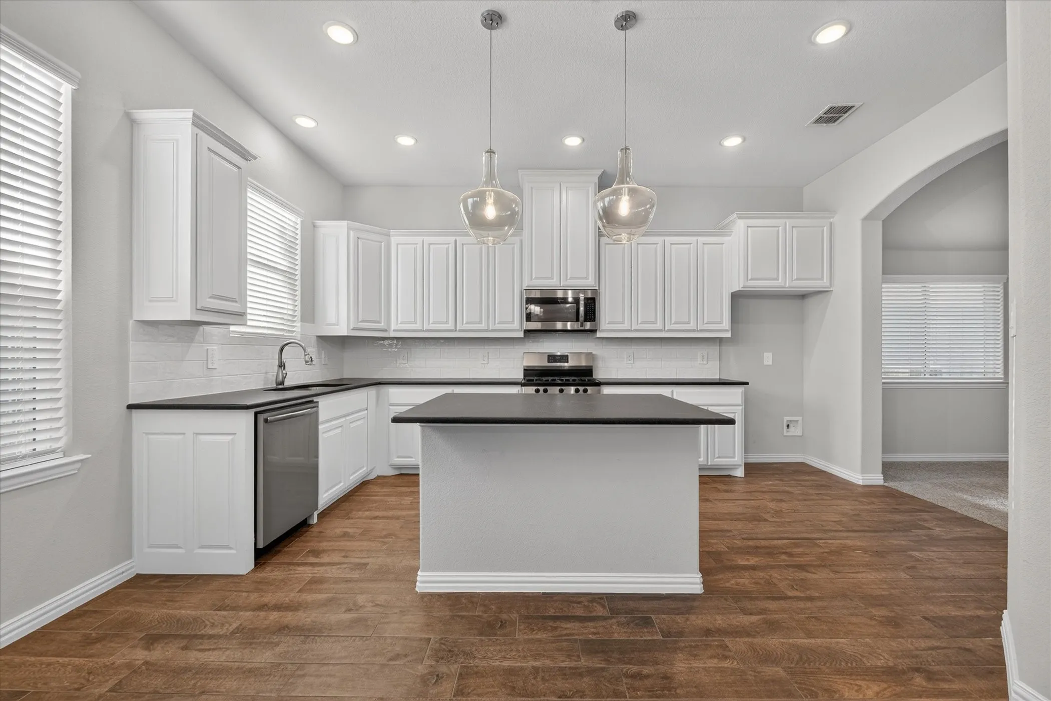 White cabinetry, dark countertops, a central island, stainless steel appliances, and wood-finish flooring