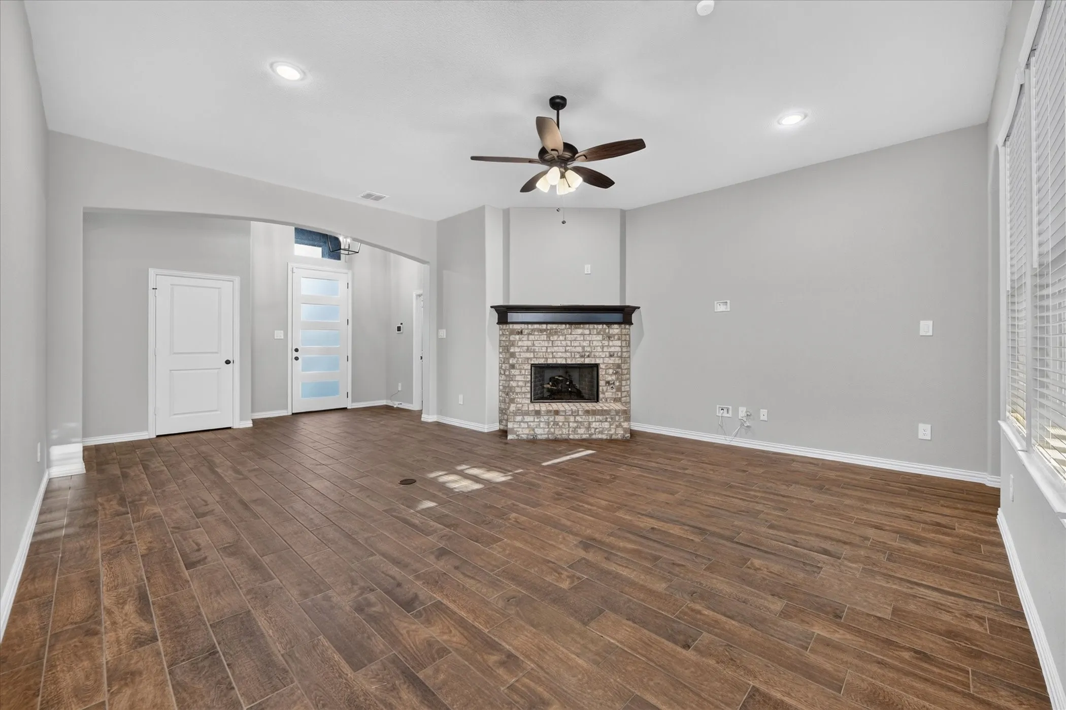 Spacious interior featuring wood-finish flooring, a brick fireplace with a dark wood mantel, and an entry door with frosted glass panels