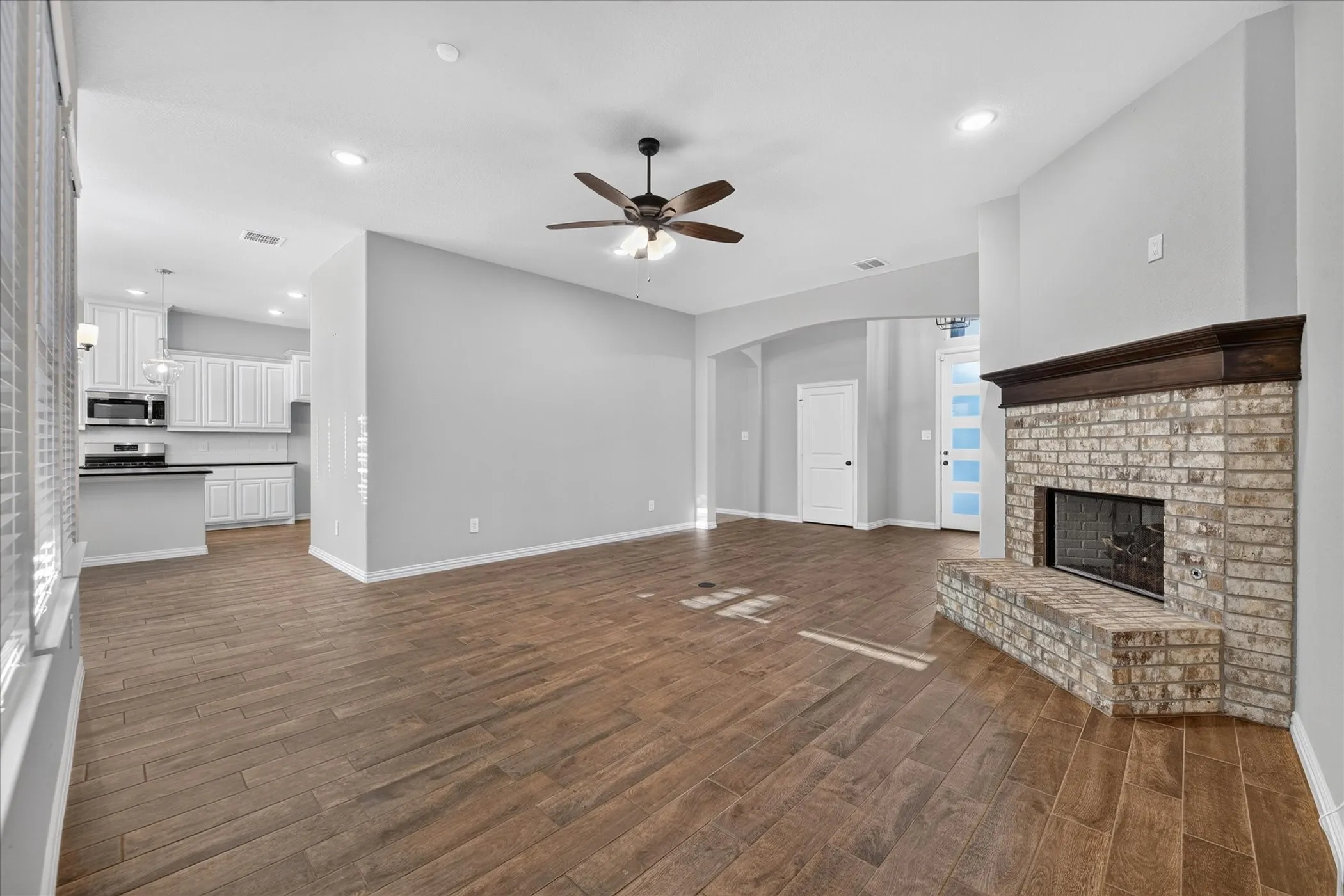 Living area featuring wood-finish flooring, a brick fireplace with a wood mantle, and a ceiling fan