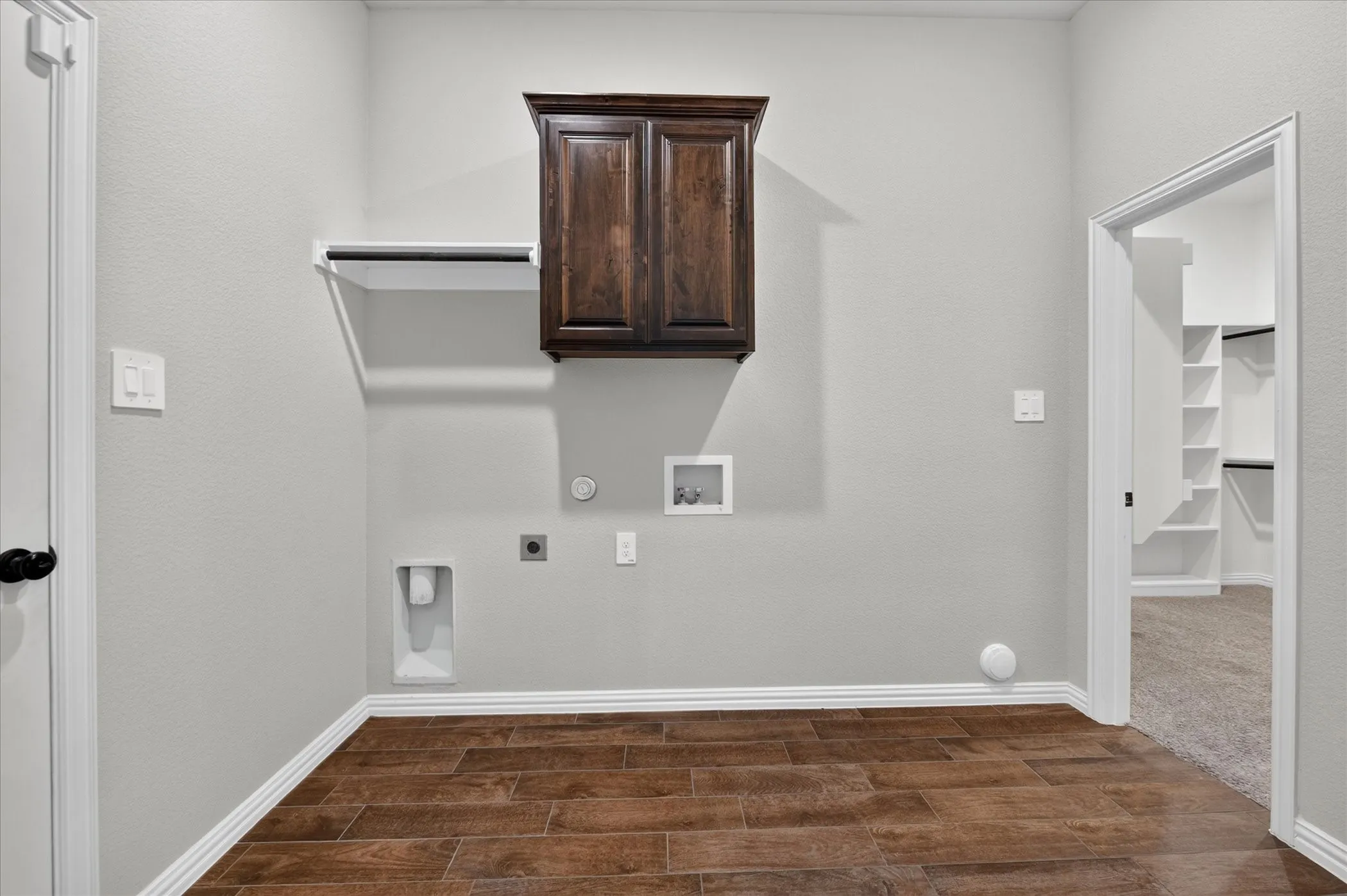 Wood-finish flooring, overhead shelving, dark wood-finish cabinetry, and laundry hookups