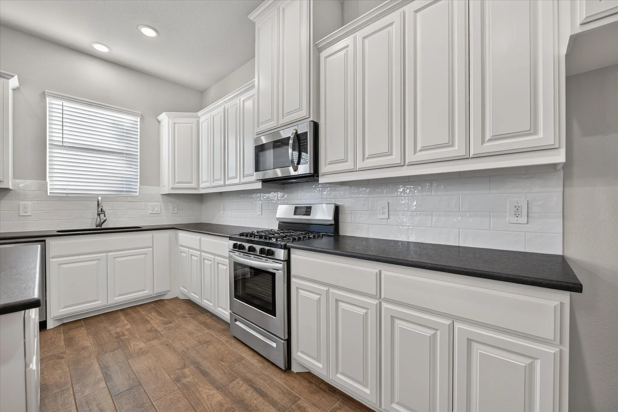 White shaker-style cabinetry, dark countertops, subway tile backsplash, stainless steel appliances, and wood-finish flooring