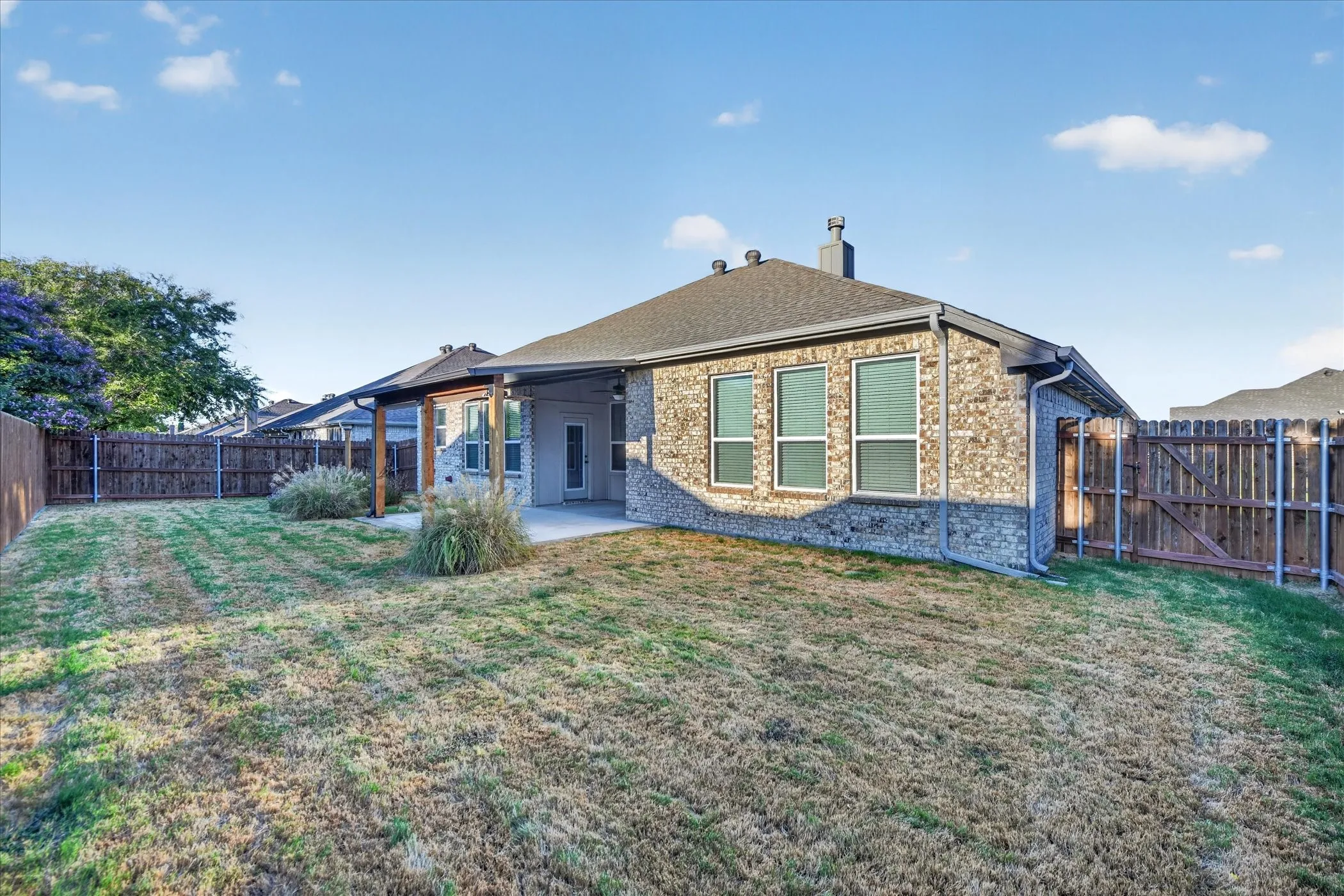 Brick and stone exterior with a covered patio, multiple windows, and a wood fence enclosing the perimeter