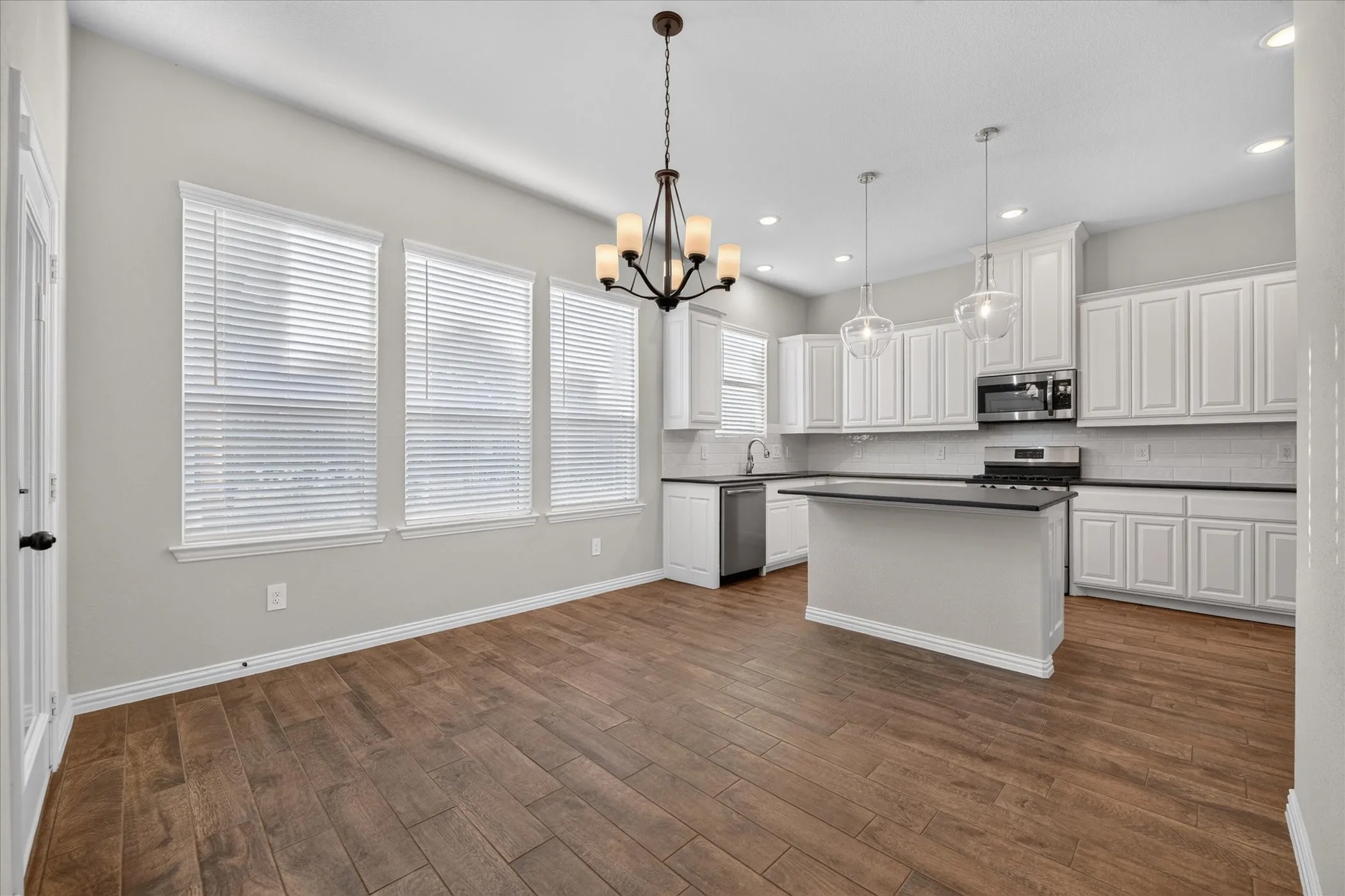 Kitchen area featuring wood-finish flooring, white cabinetry, a kitchen island, and stainless steel appliances