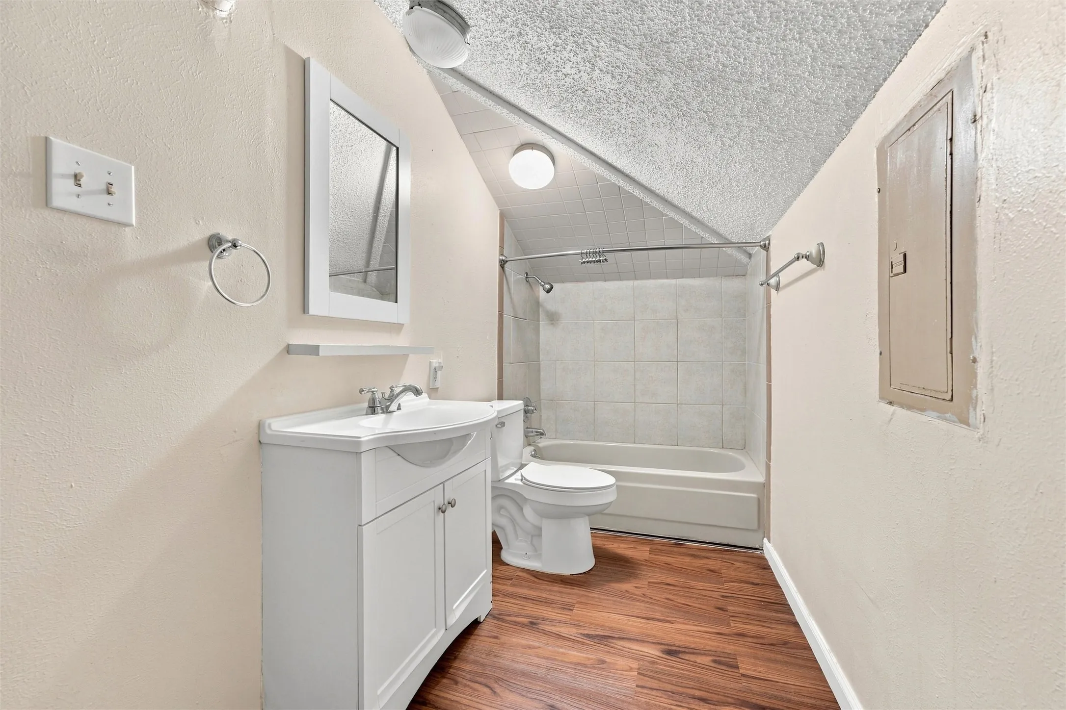 White vanity with integrated sink, chrome faucet, wall-mounted mirror, and wood-finish flooring
