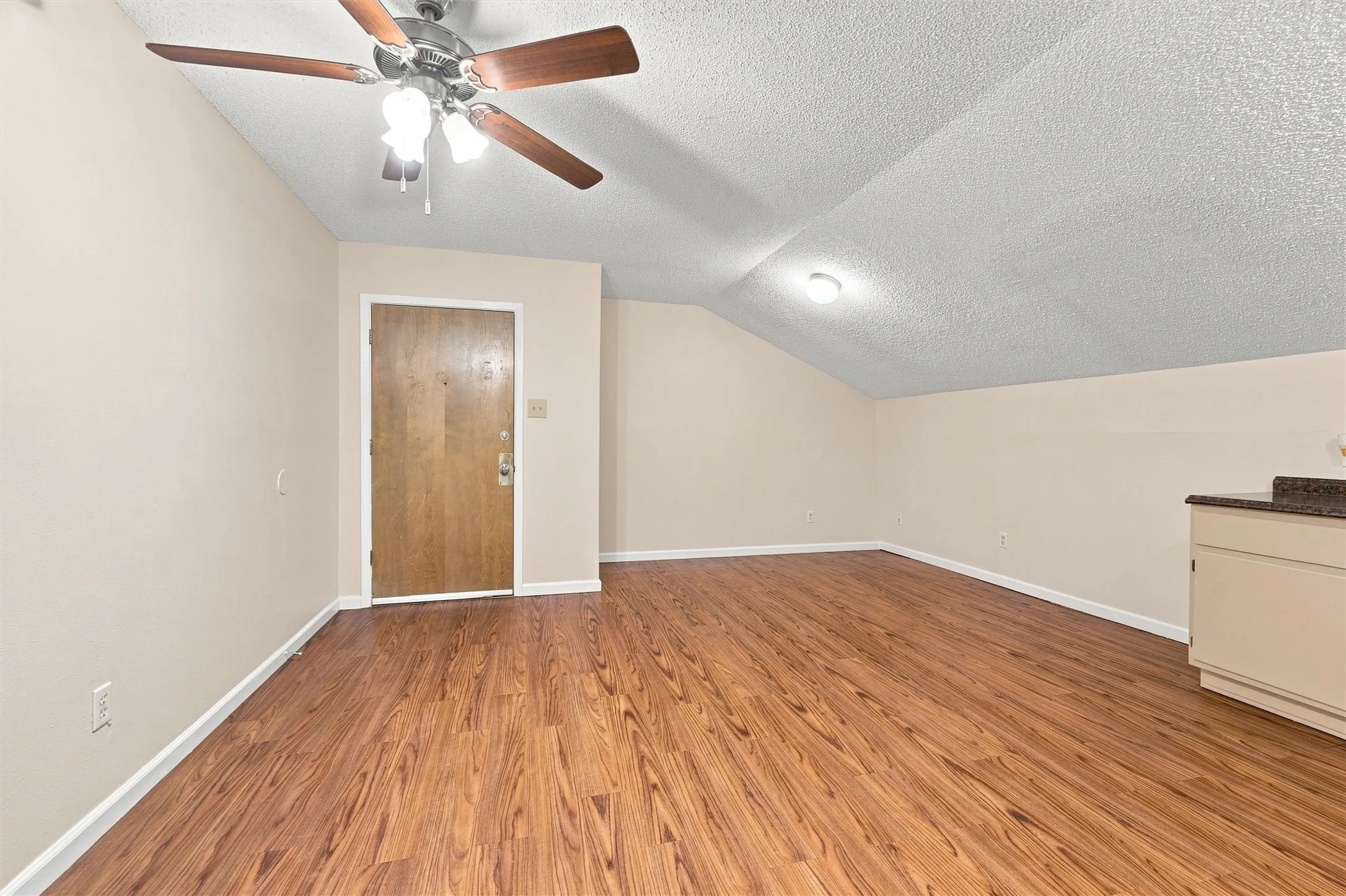 Wood-finish flooring, an angled ceiling, a ceiling fan with light fixture, and built-in cabinetry with a countertop
