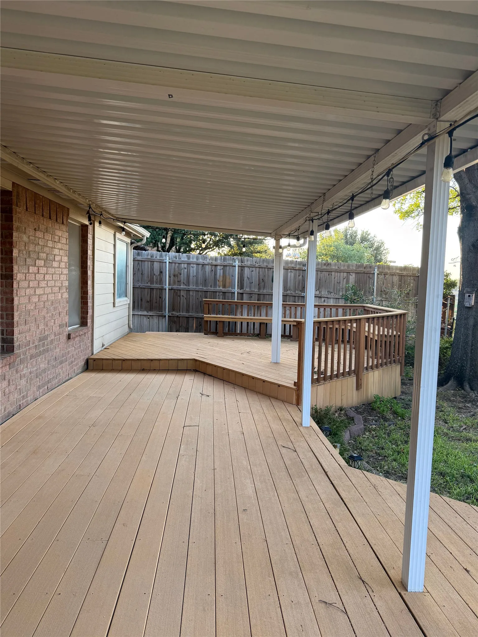Expansive wood-finish deck with multiple levels, a built-in bench, and protective railing, all under a covered patio structure