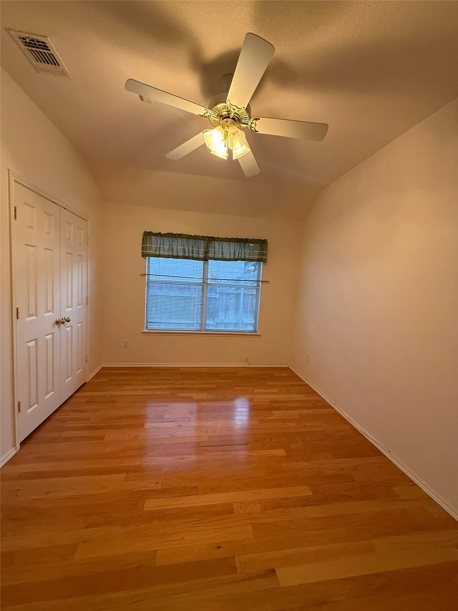 Wood-finish flooring, vaulted ceiling, ceiling fan with integrated lighting, window with window treatment, and a two-panel bi-fold closet door