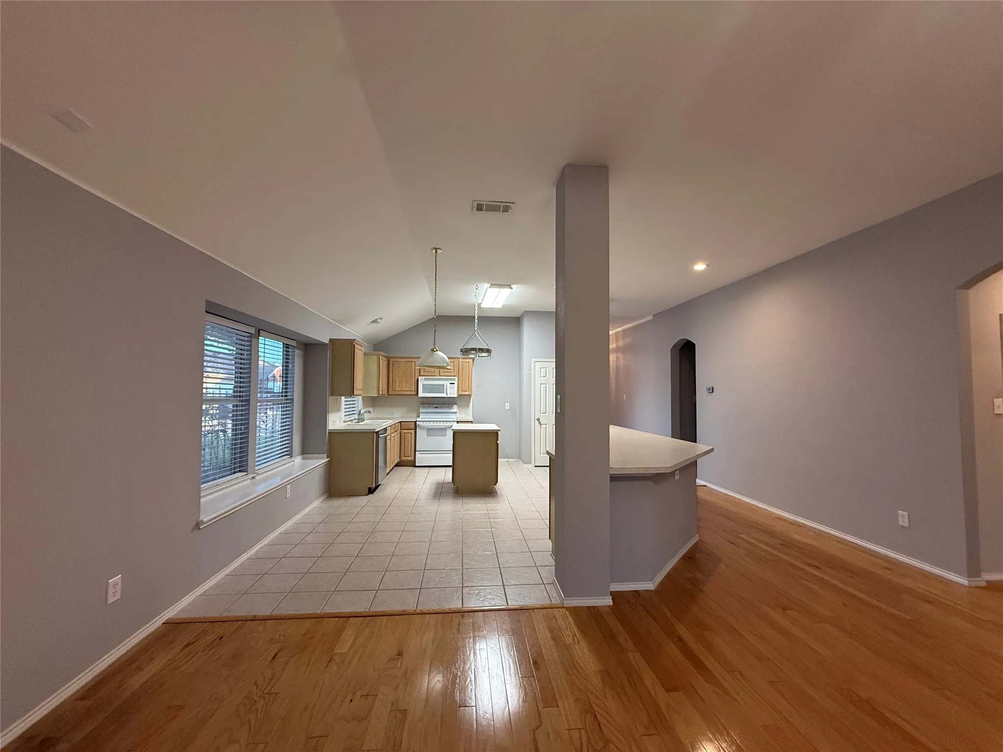 Wood-finish flooring, vaulted ceiling, recessed lighting, kitchen island, and light wood cabinetry