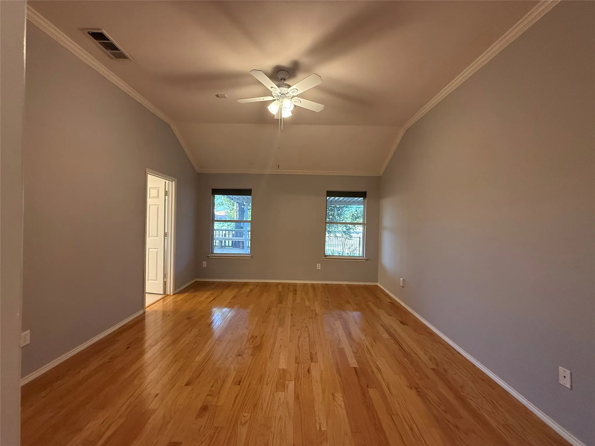 Room featuring vaulted ceilings, wood-finish flooring, a ceiling fan, and two windows