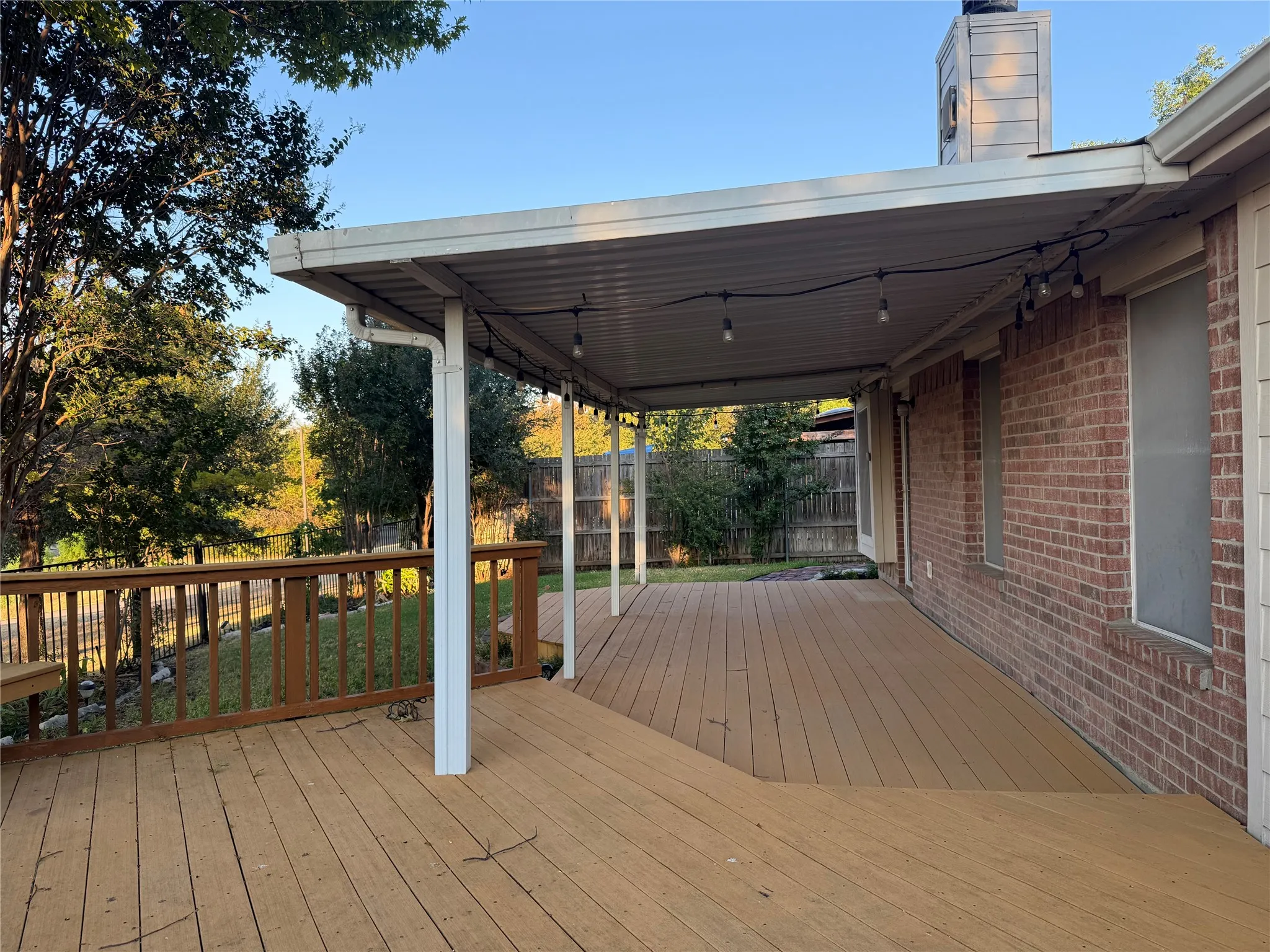 Expansive wood-finish deck with a built-in bench, covered patio, and brick exterior