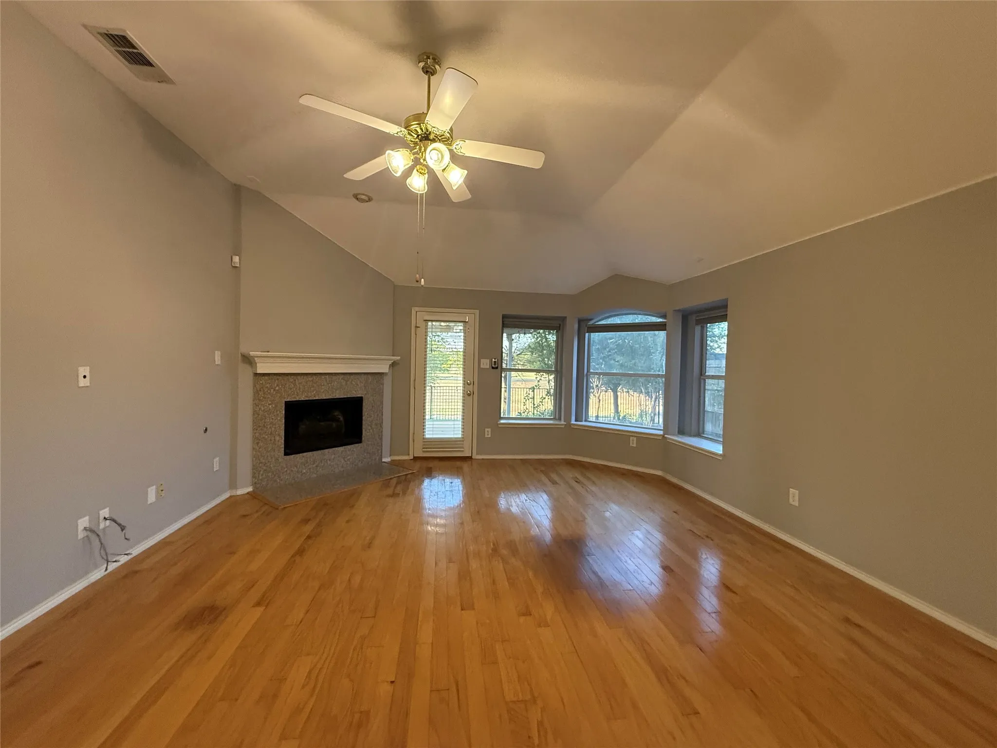 Vaulted ceiling, wood-finish flooring, fireplace with tile surround, ceiling fan, and bay windows