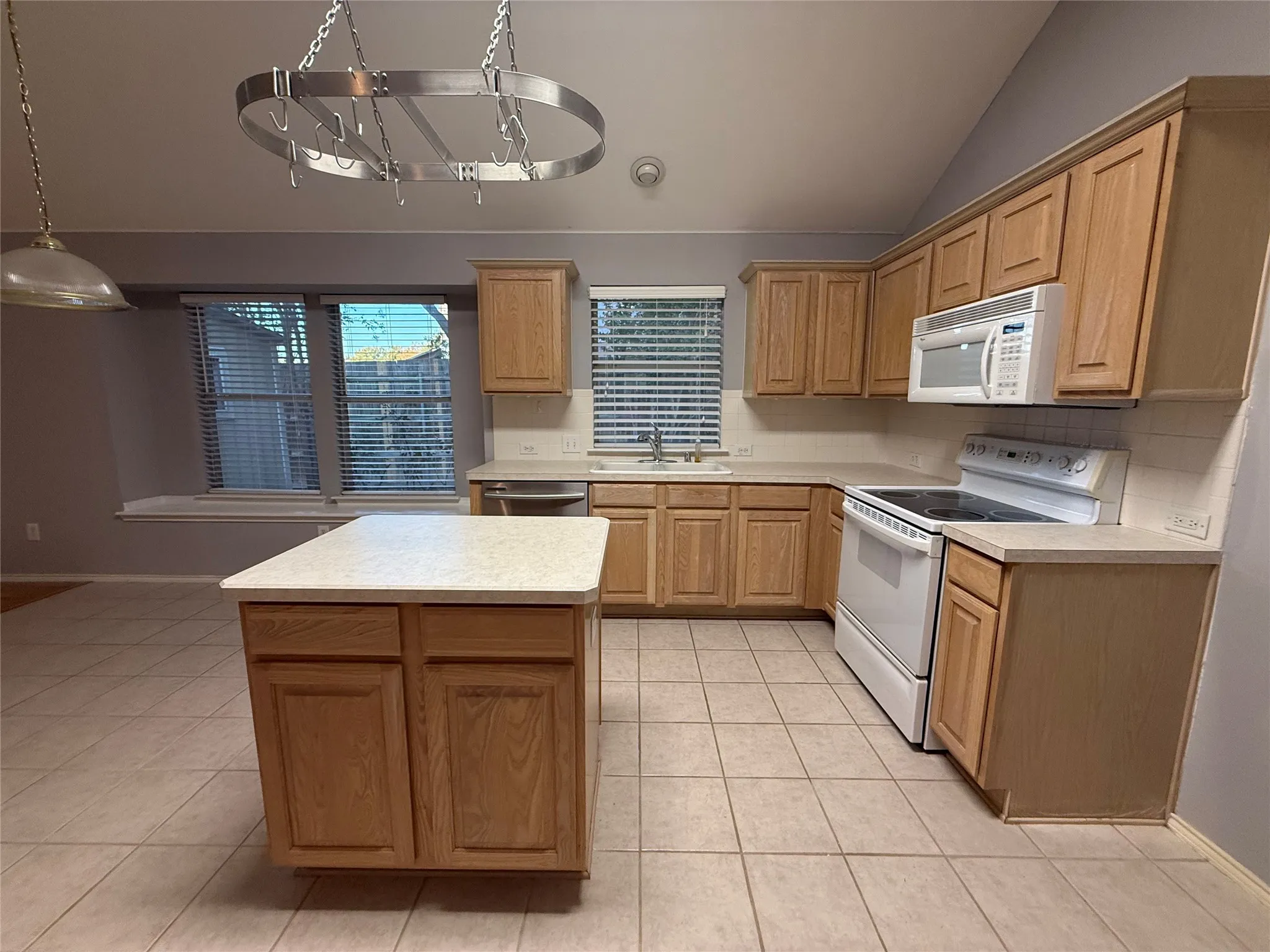 Kitchen featuring vaulted ceilings, wood cabinetry, a central island, tile flooring, and white appliances