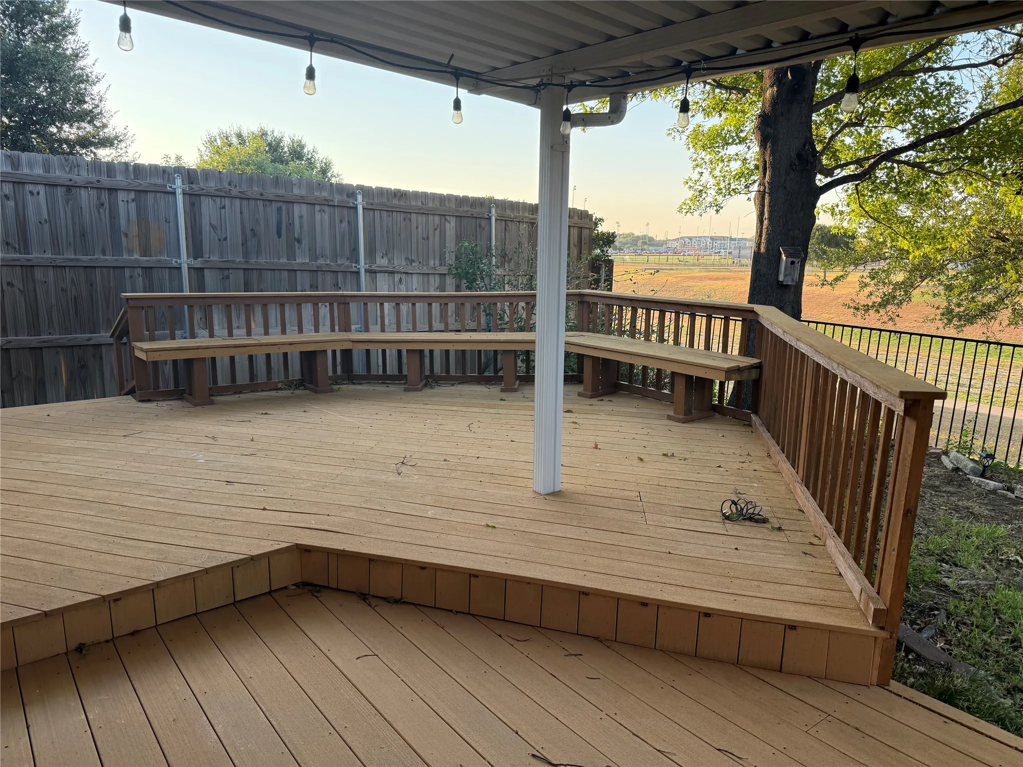 Expansive wood deck with built-in bench seating, wood railing, and string lighting, complemented by a corrugated metal patio cover