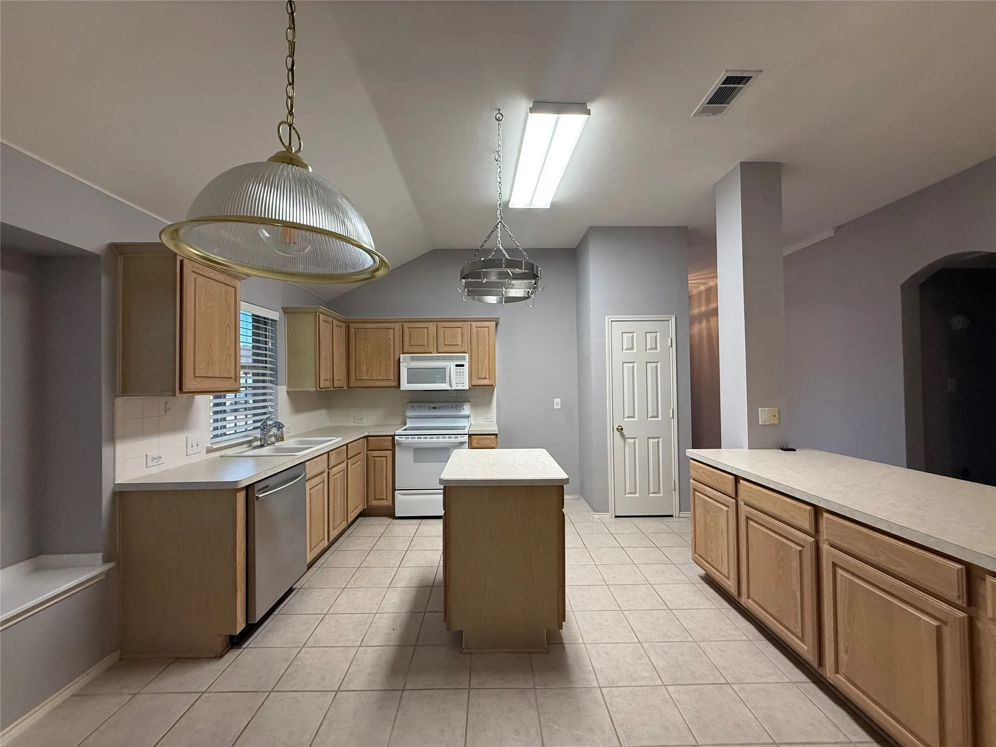 Kitchen featuring light wood-finish cabinetry, a built-in kitchen island, a white appliance package, and ceramic tile flooring