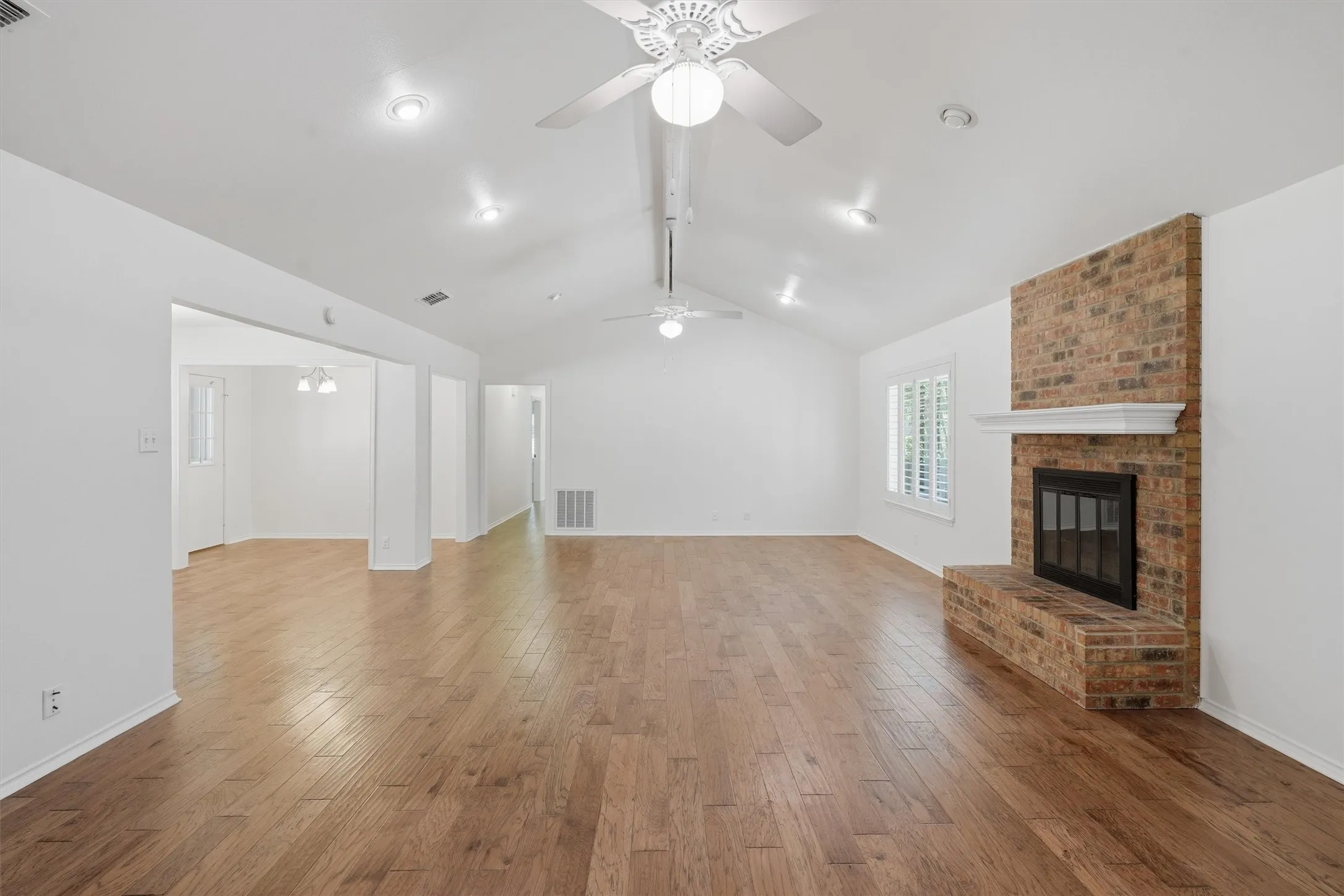 Spacious interior featuring wood-finish flooring, a brick fireplace with mantel, and white interior shutters