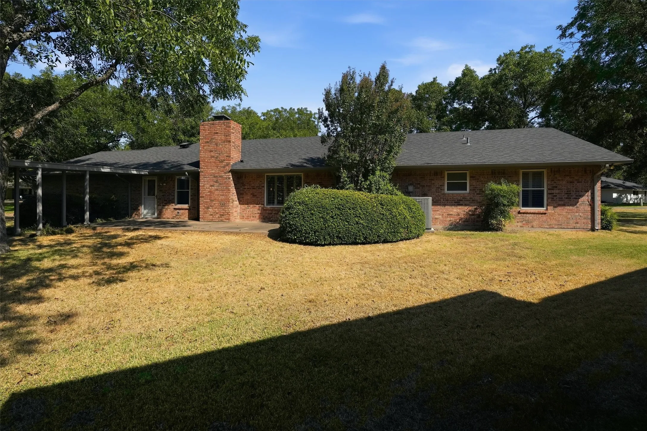 Brick exterior with dark shingle roofing, screened-in porch, and a brick chimney