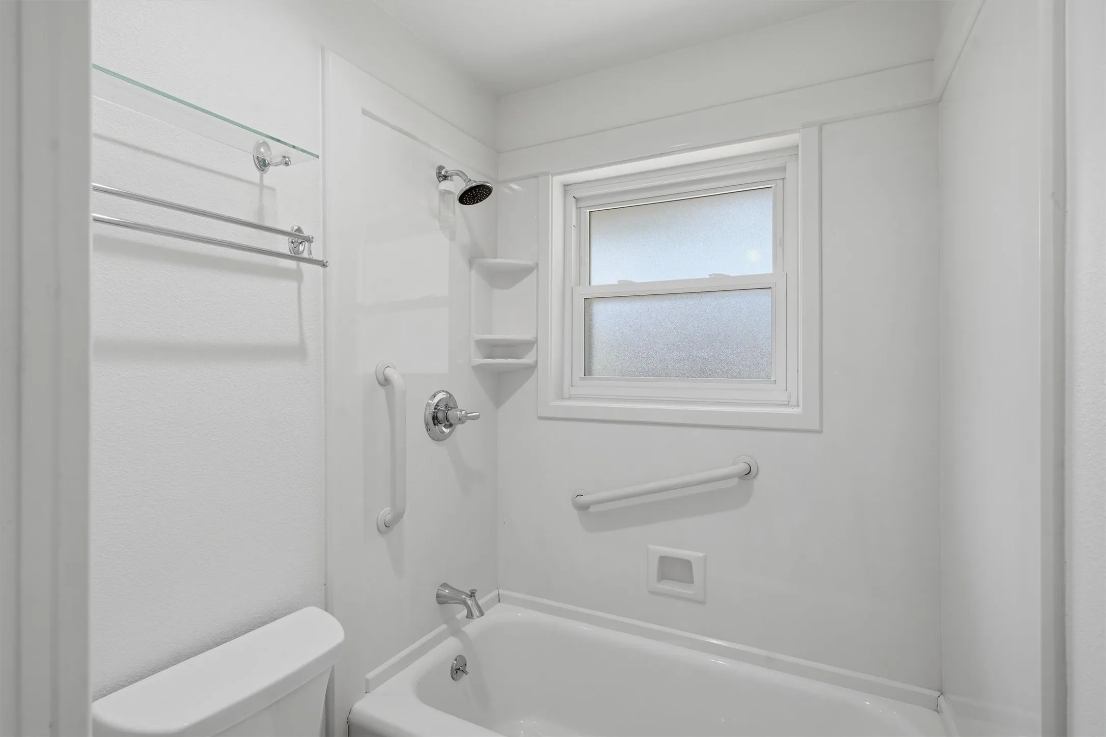 White shower/tub combination with chrome fixtures, an integrated shower caddy, and a window