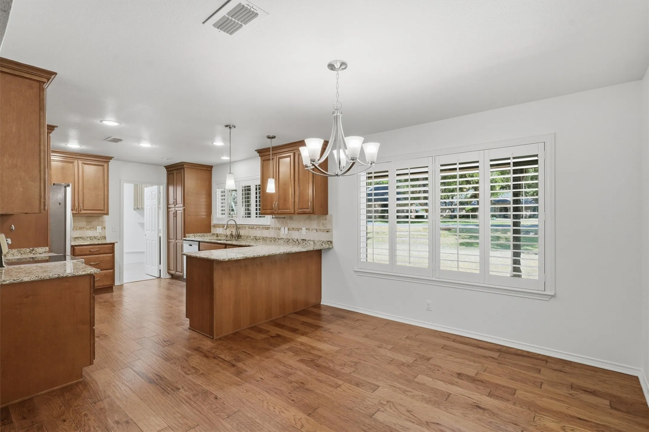 Open-concept kitchen and dining area featuring wood-finish flooring, custom wood cabinetry, and granite countertops