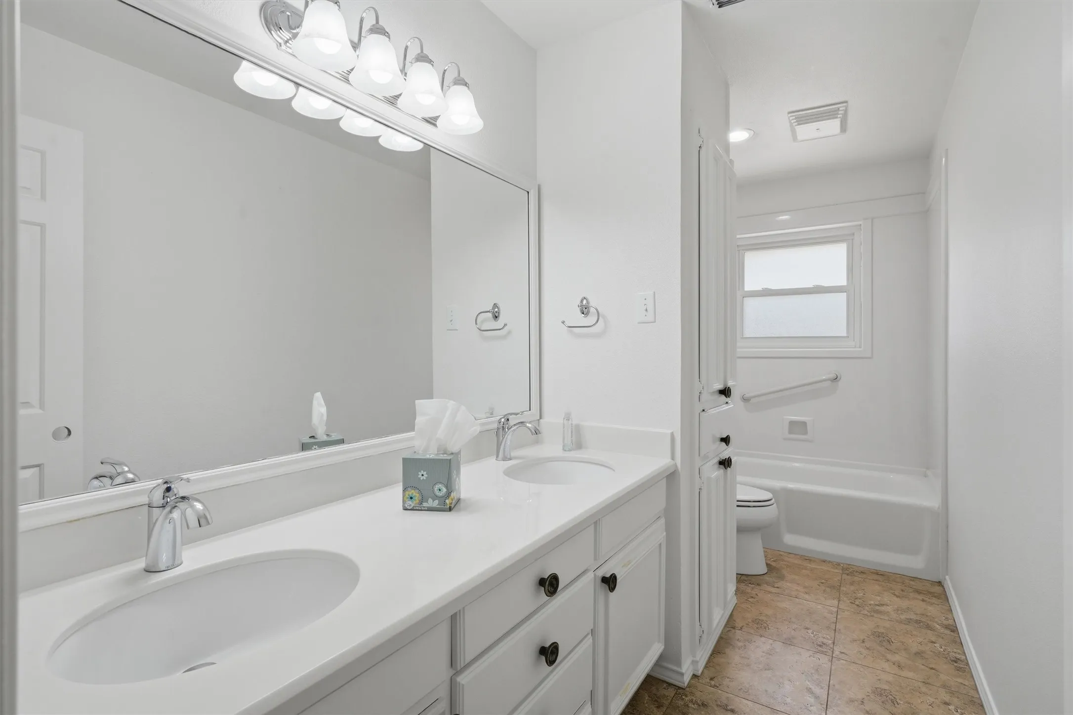 Dual vanity with white cabinetry, polished chrome fixtures, and a large wall-mounted mirror
