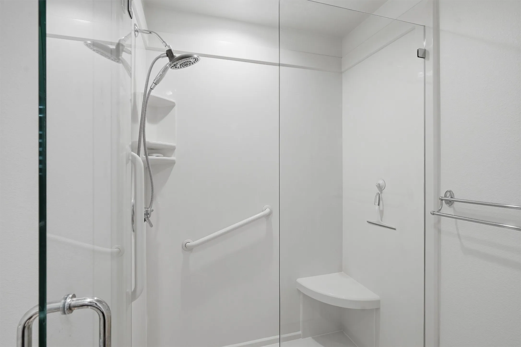 Shower enclosure with clear glass panel, built-in seating, integrated shelving, and a handheld shower fixture